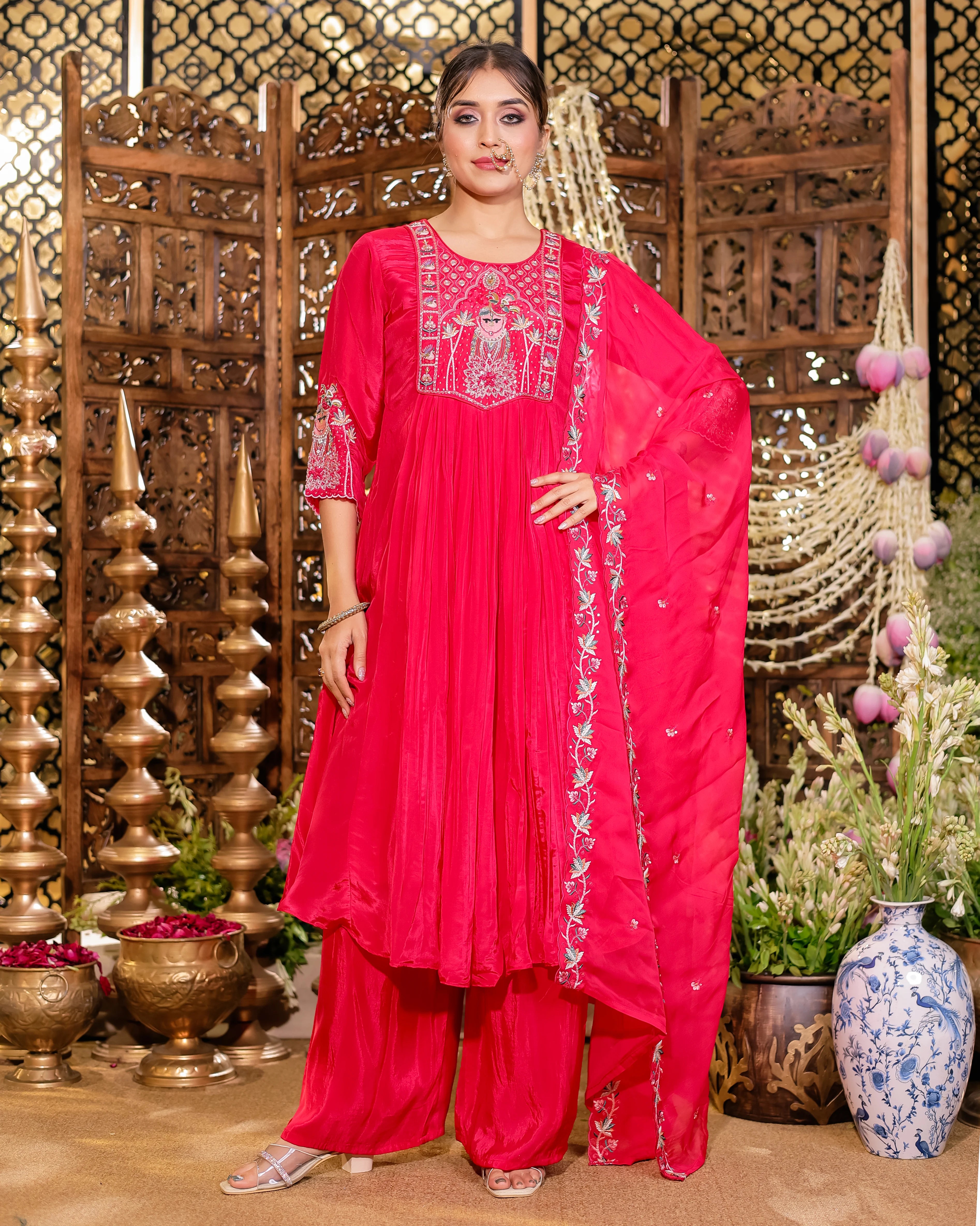 Woman in a bright pink traditional outfit with intricate patterns standing in a decorative setting.