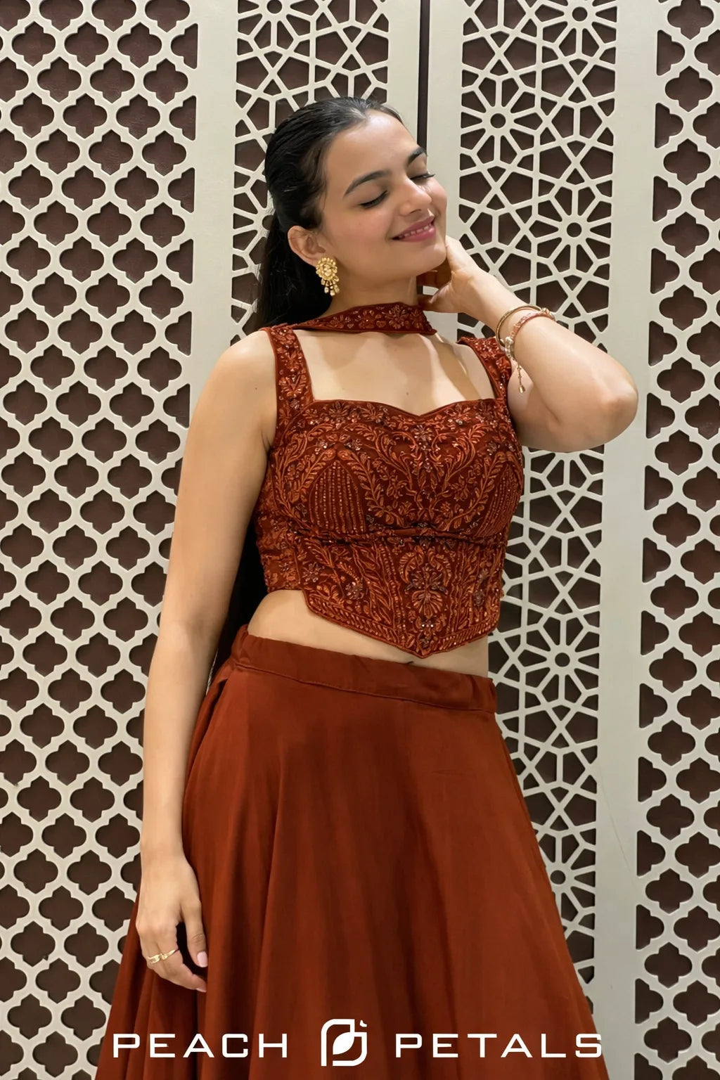 Woman wearing a rust-colored top and skirt against a patterned wall with 'Peach Petals' branding.