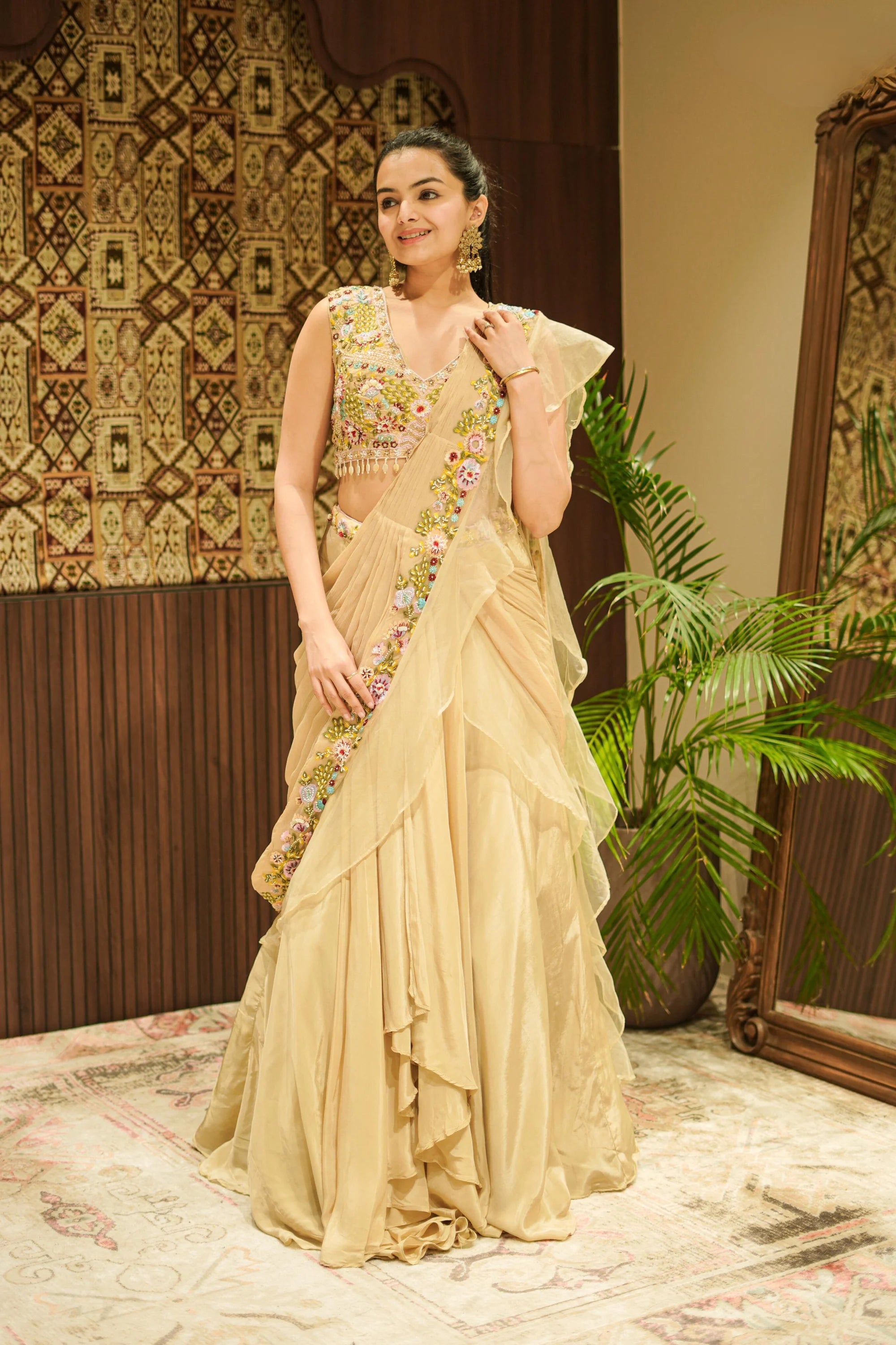Woman in a traditional beige saree with floral patterns in an indoor setting.