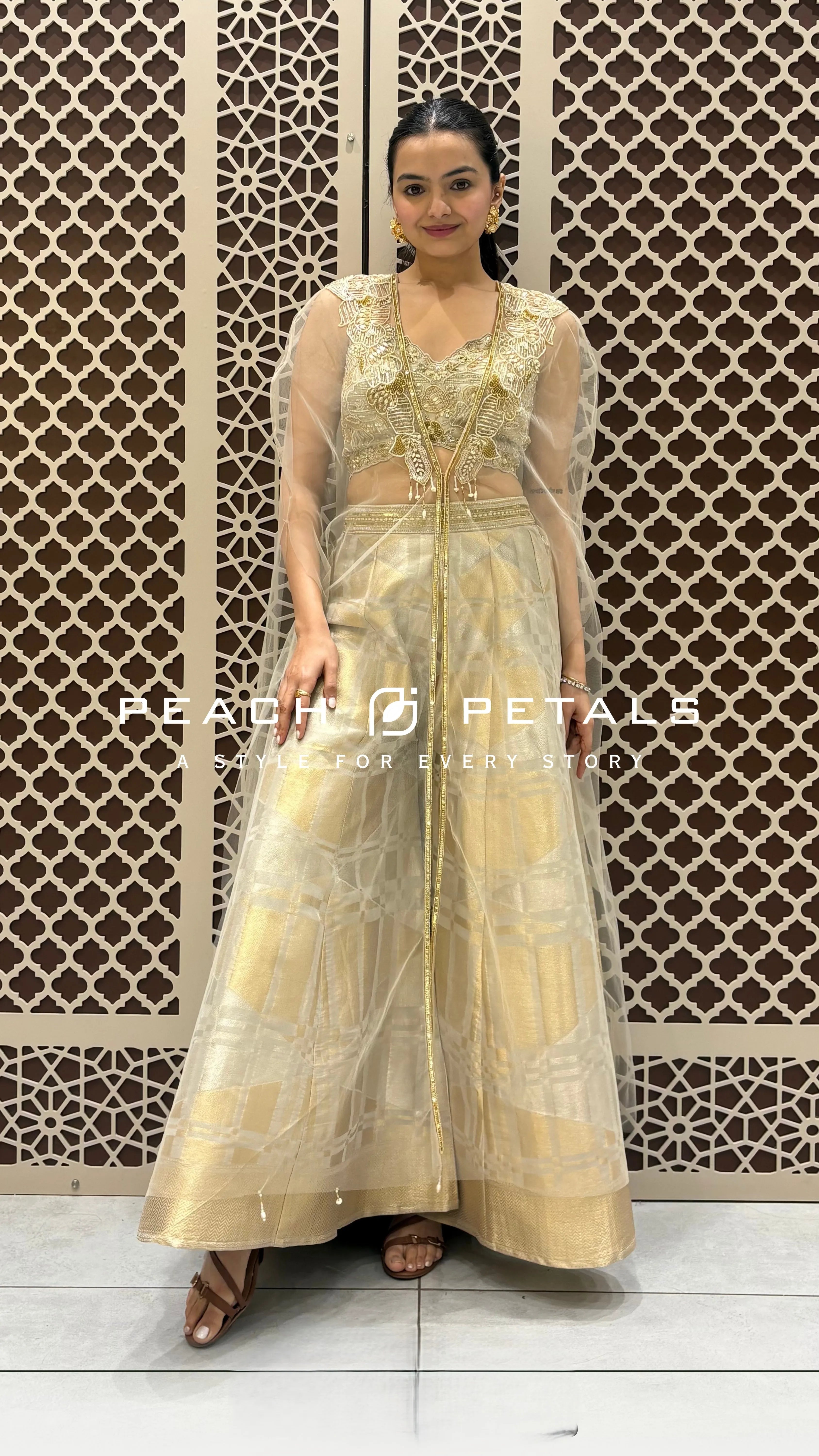 Gold checkered wide-leg trousers paired with a pearl-embellished crop top and a sheer ivory cape.