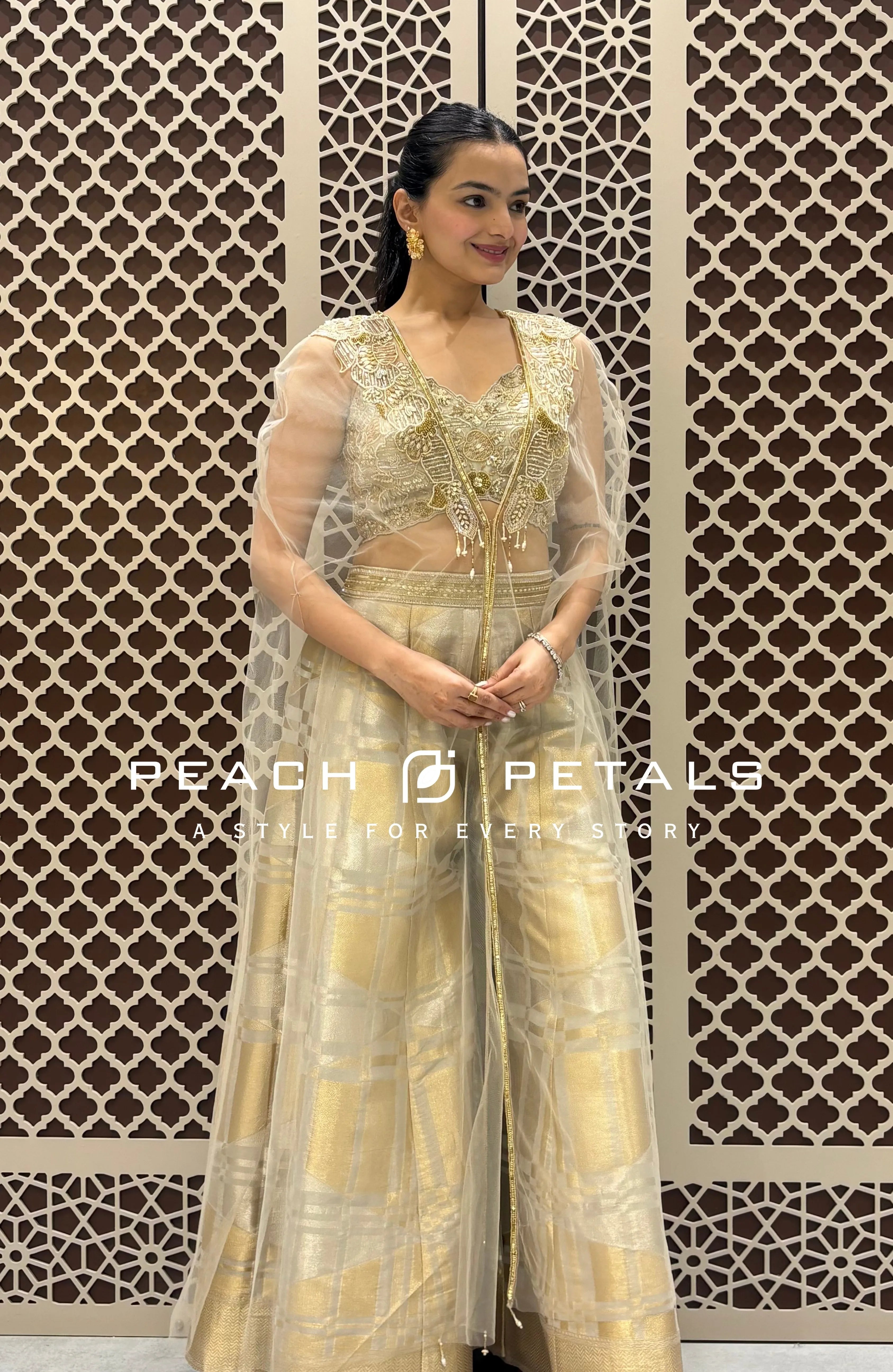 Gold checkered wide-leg trousers paired with a pearl-embellished crop top and a sheer ivory cape.