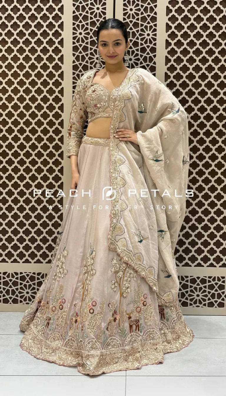 Light peach lehenga featuring detailed garden-themed embroidery with bird and deer motifs and scalloped dupatta.