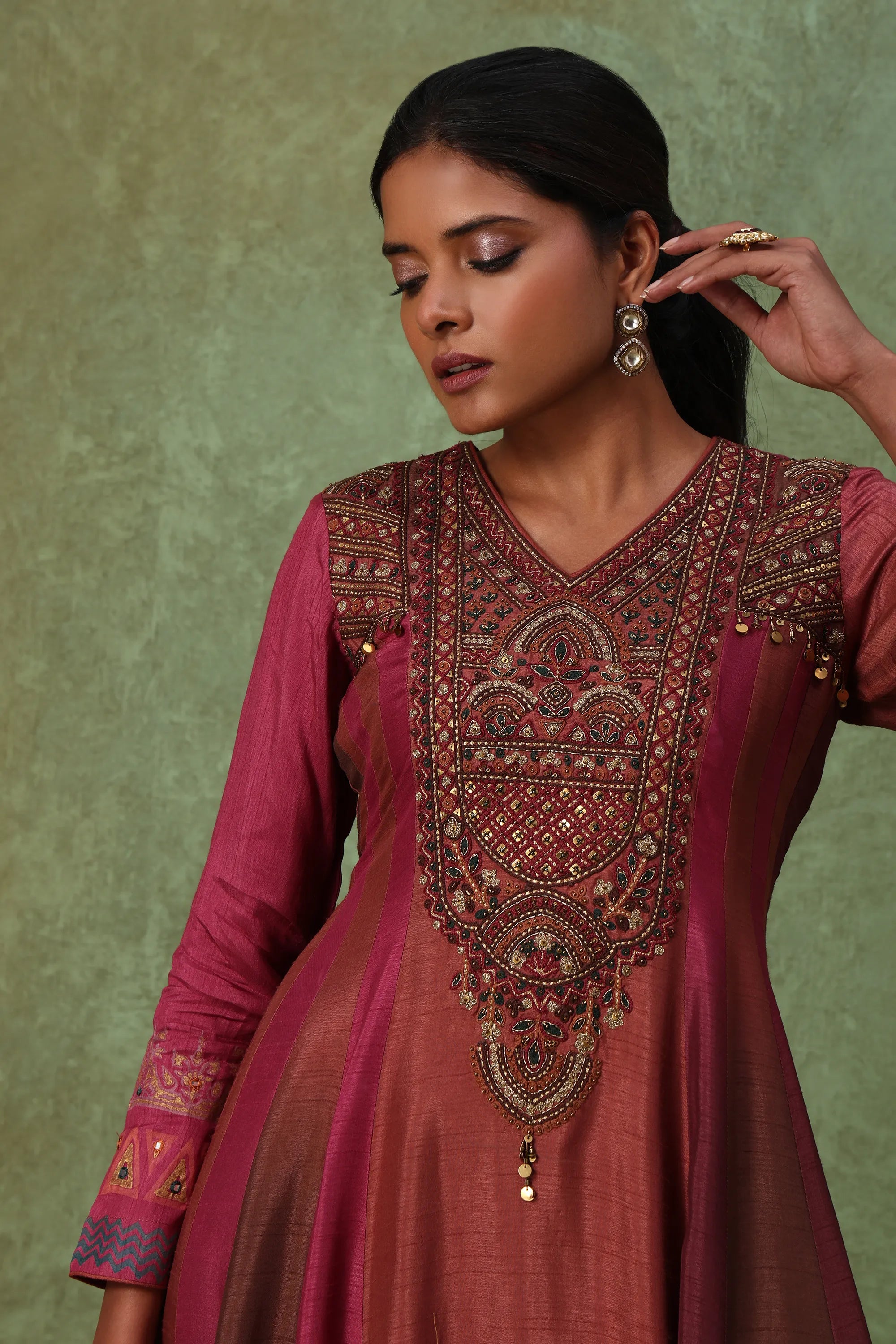 Woman wearing a maroon traditional outfit with intricate embroidery against a green background