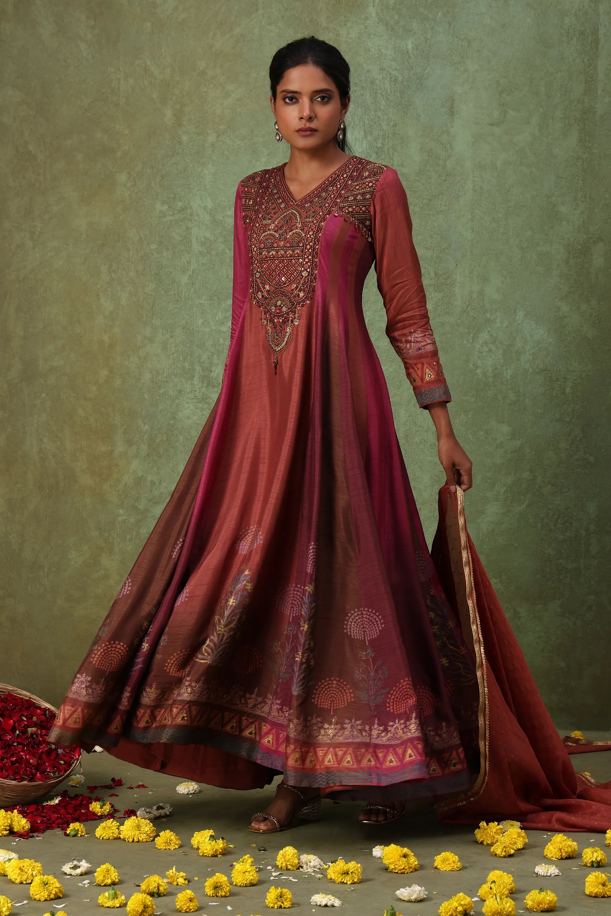 Woman in a traditional maroon dress with intricate patterns on a textured green background