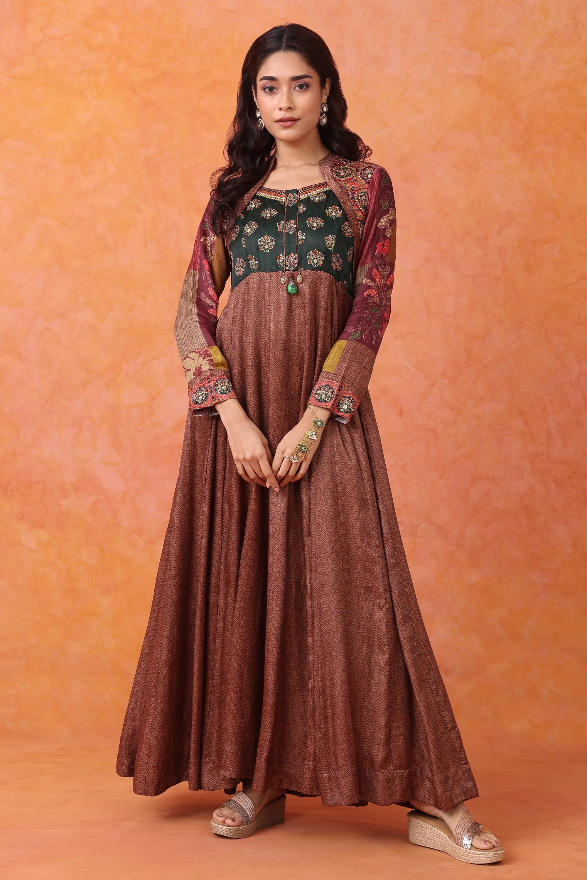 Woman wearing a long brown dress with floral top against an orange background