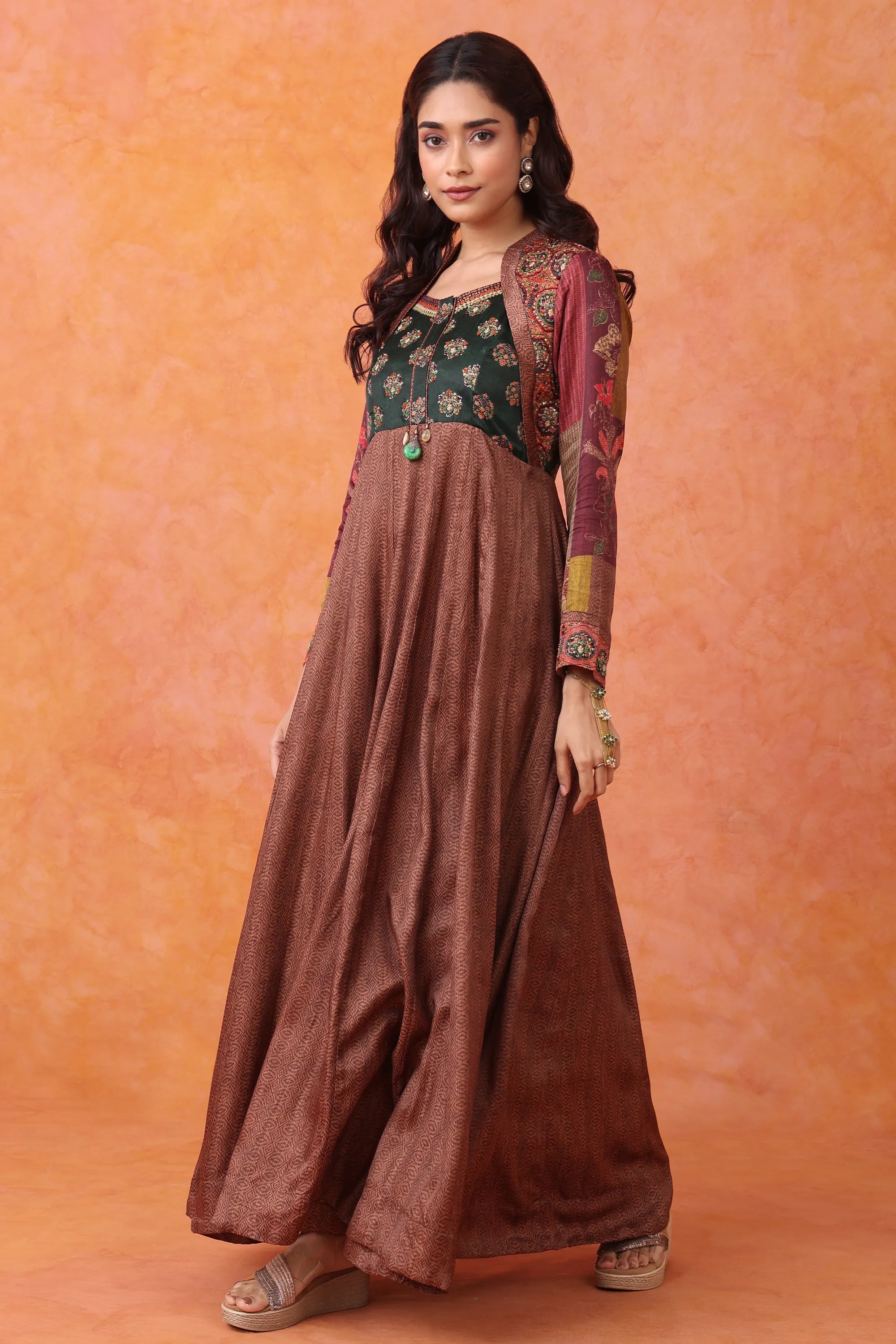 Woman wearing a traditional outfit with a green top and brown pants against an orange background