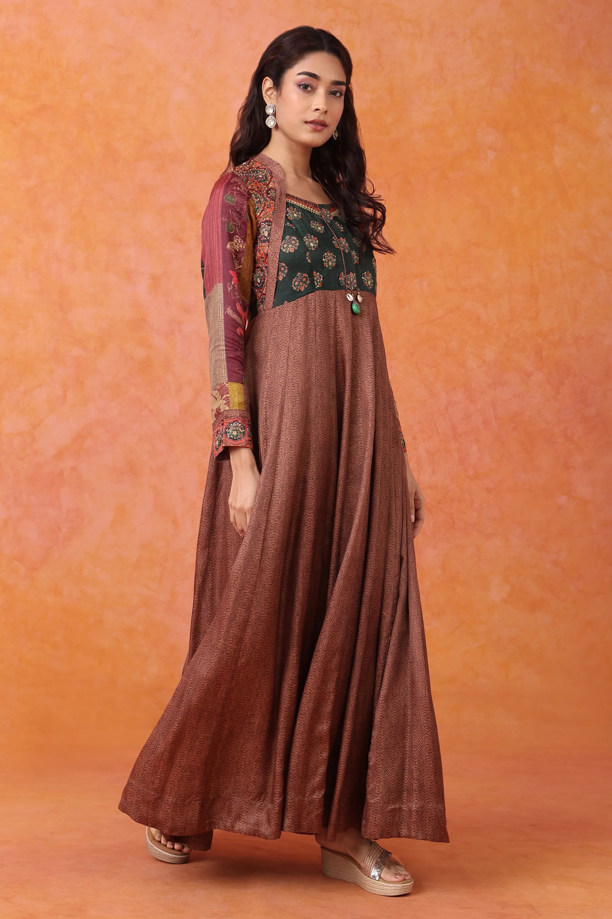 Woman wearing a traditional outfit with a brown long dress and green top against an orange background