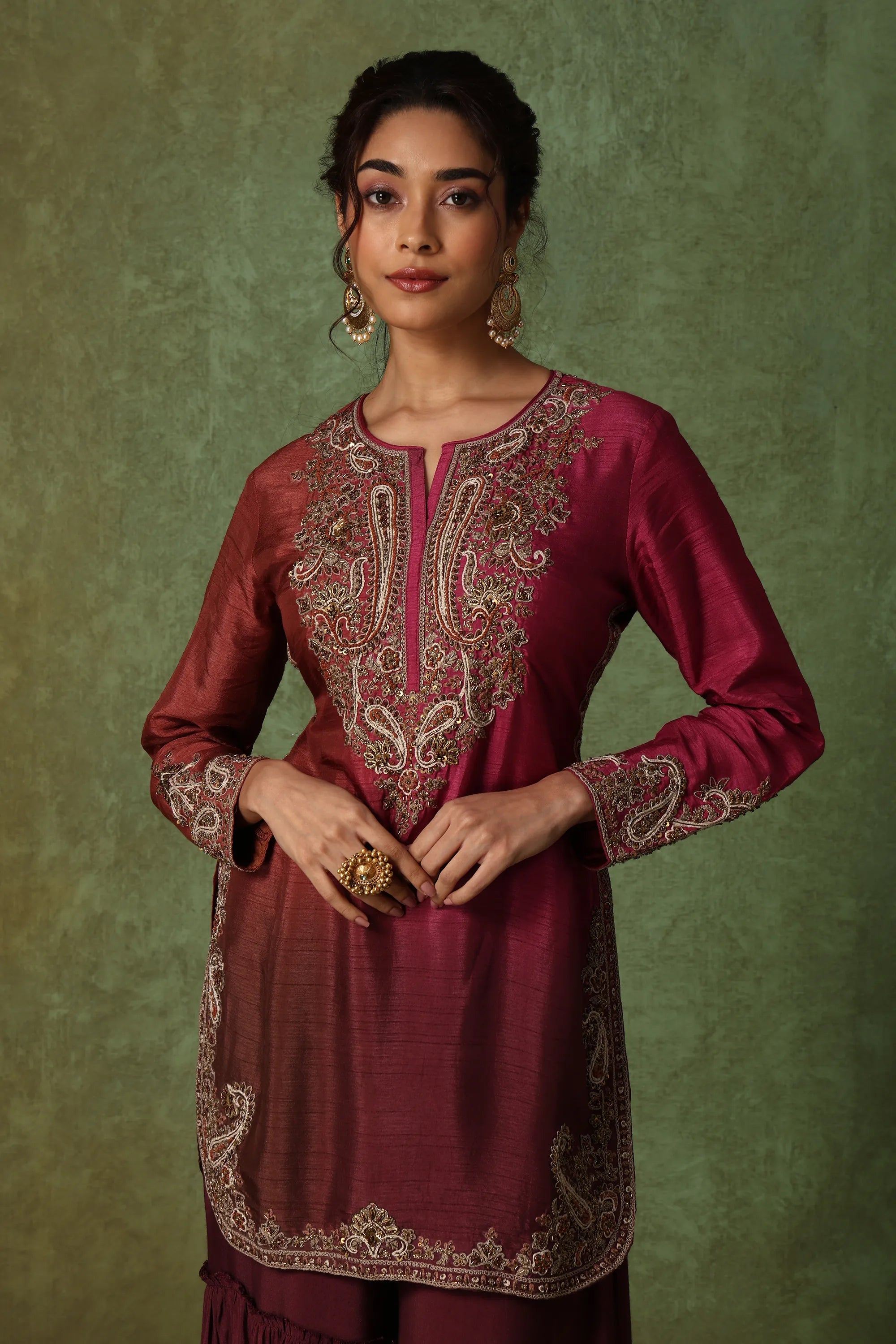 Woman wearing a maroon embroidered traditional outfit against a green background