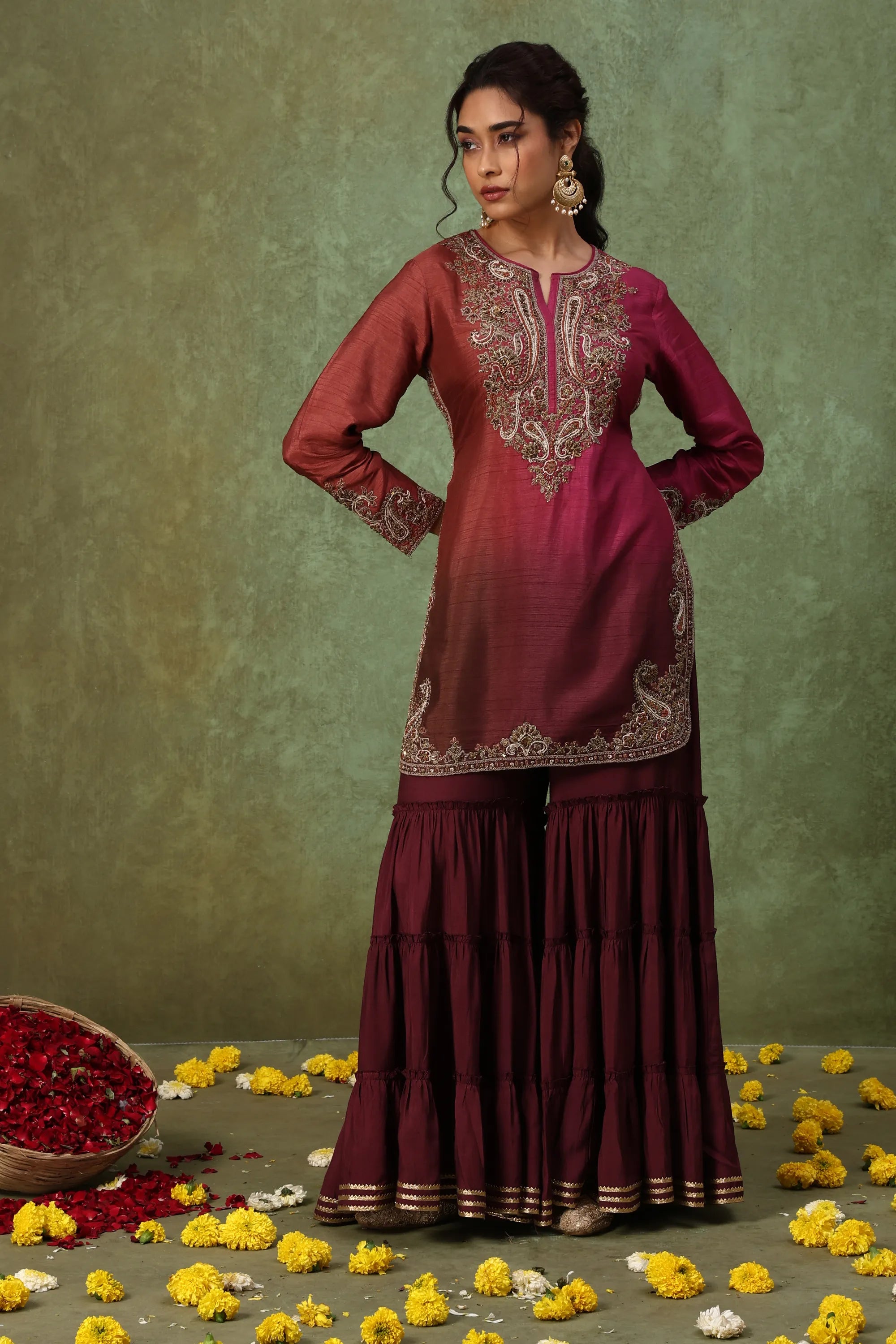 Woman wearing a maroon traditional outfit with floral decorations on a green background