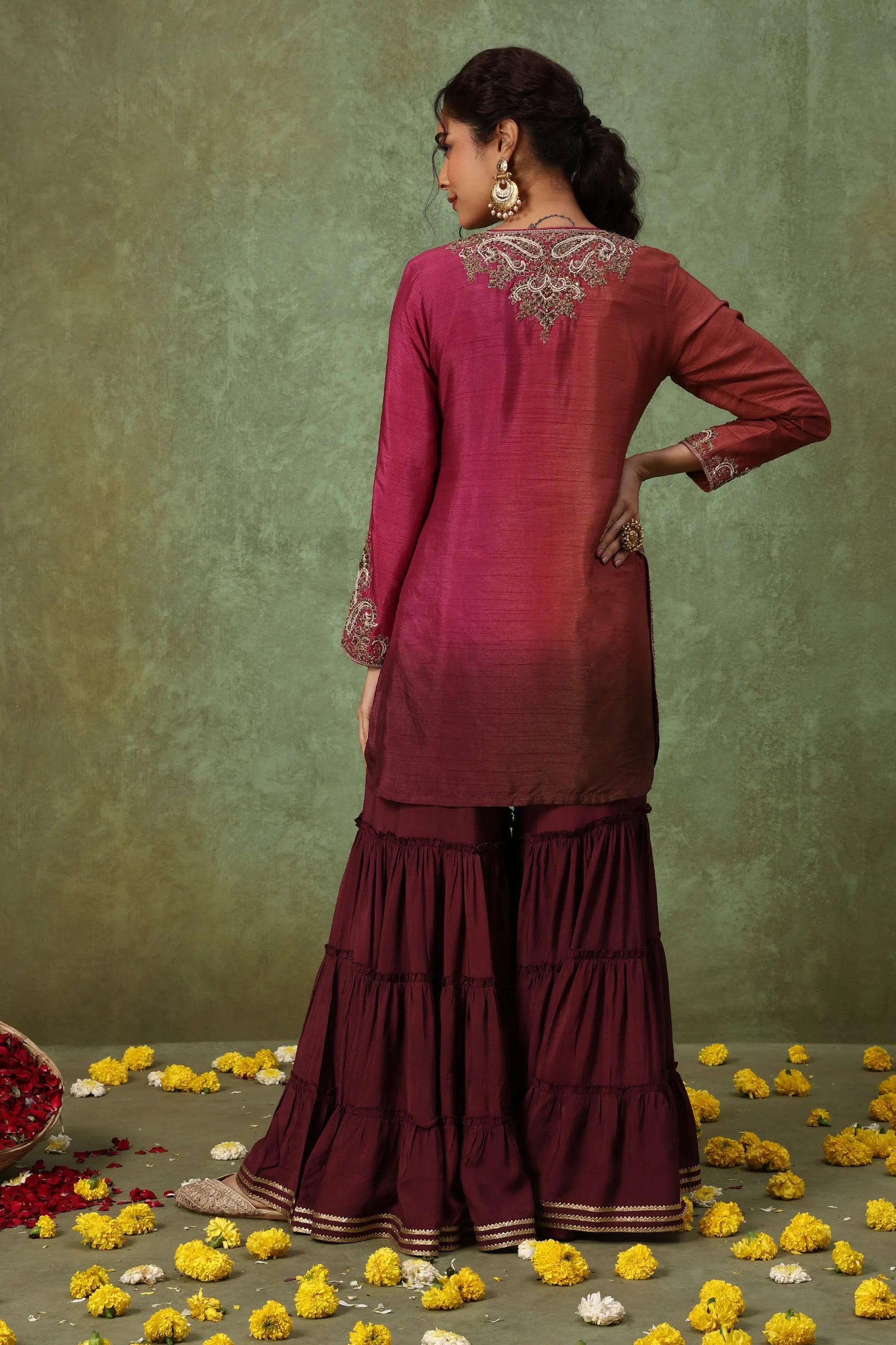 Woman wearing a maroon traditional outfit with floral decorations on a green background