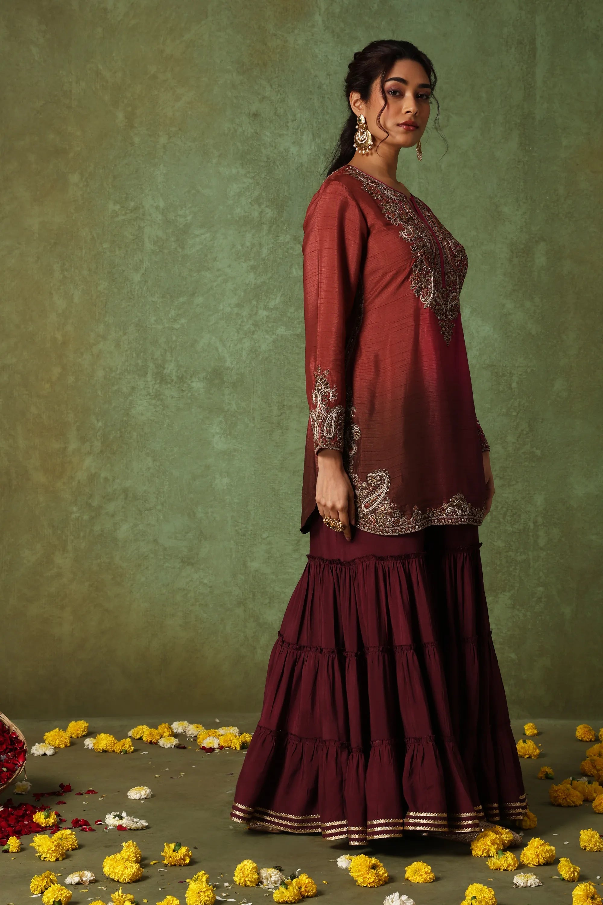 Woman in a maroon traditional outfit with floral decorations on a green background