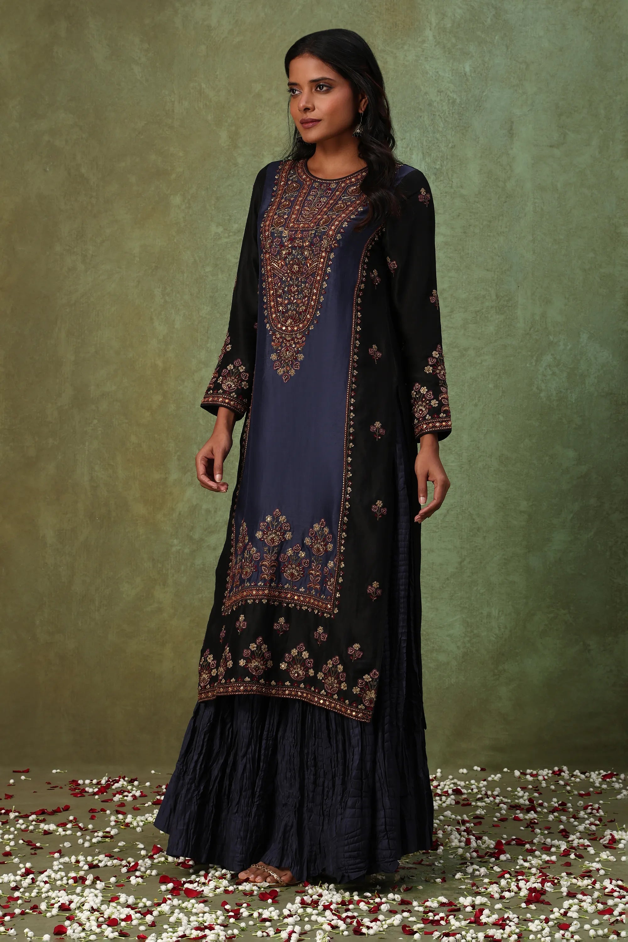 Woman wearing a black and blue embroidered traditional outfit with a green background