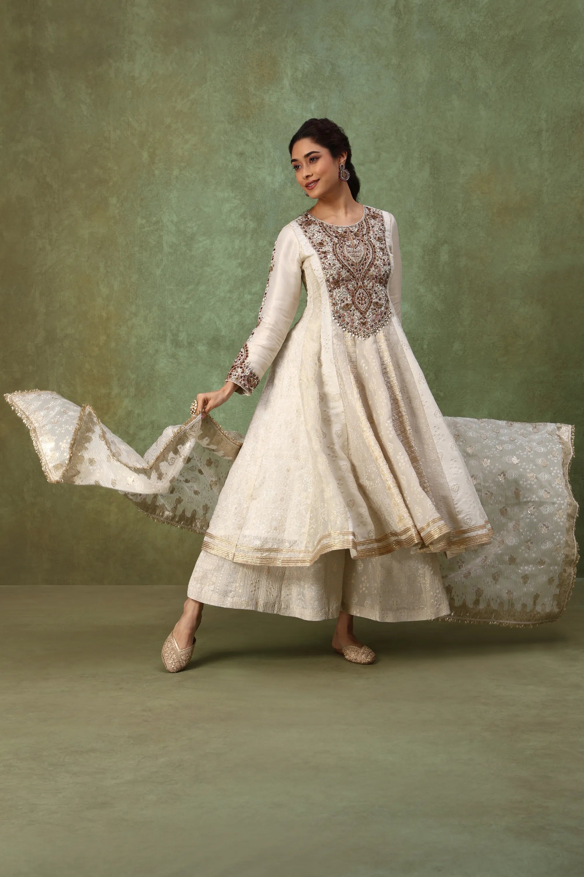 Woman in a traditional outfit with embroidered top and flowing fabric against a green background