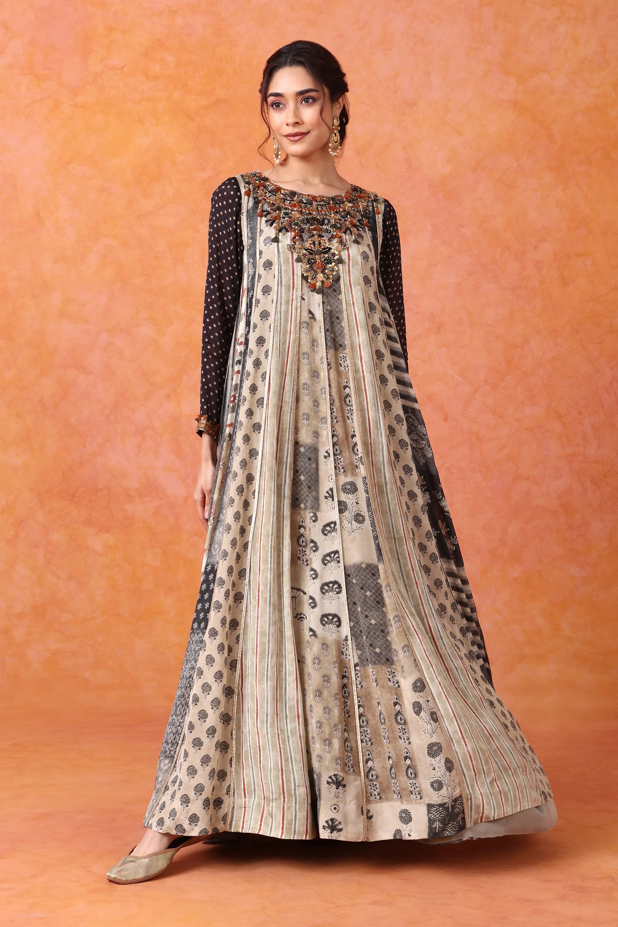 Woman wearing a patterned dress with a black top against an orange background