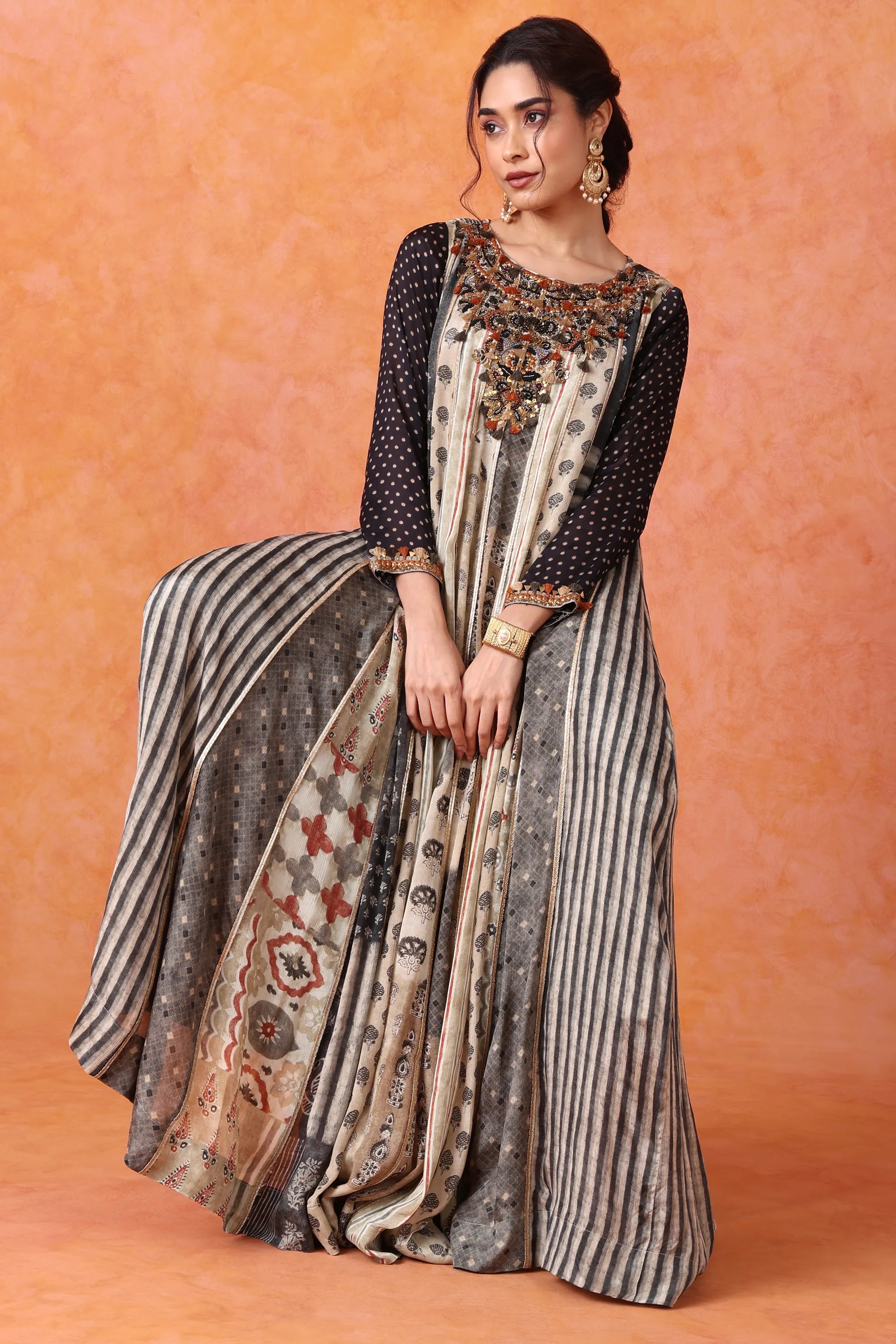 Woman wearing a long, patterned dress with a matching dupatta against an orange background