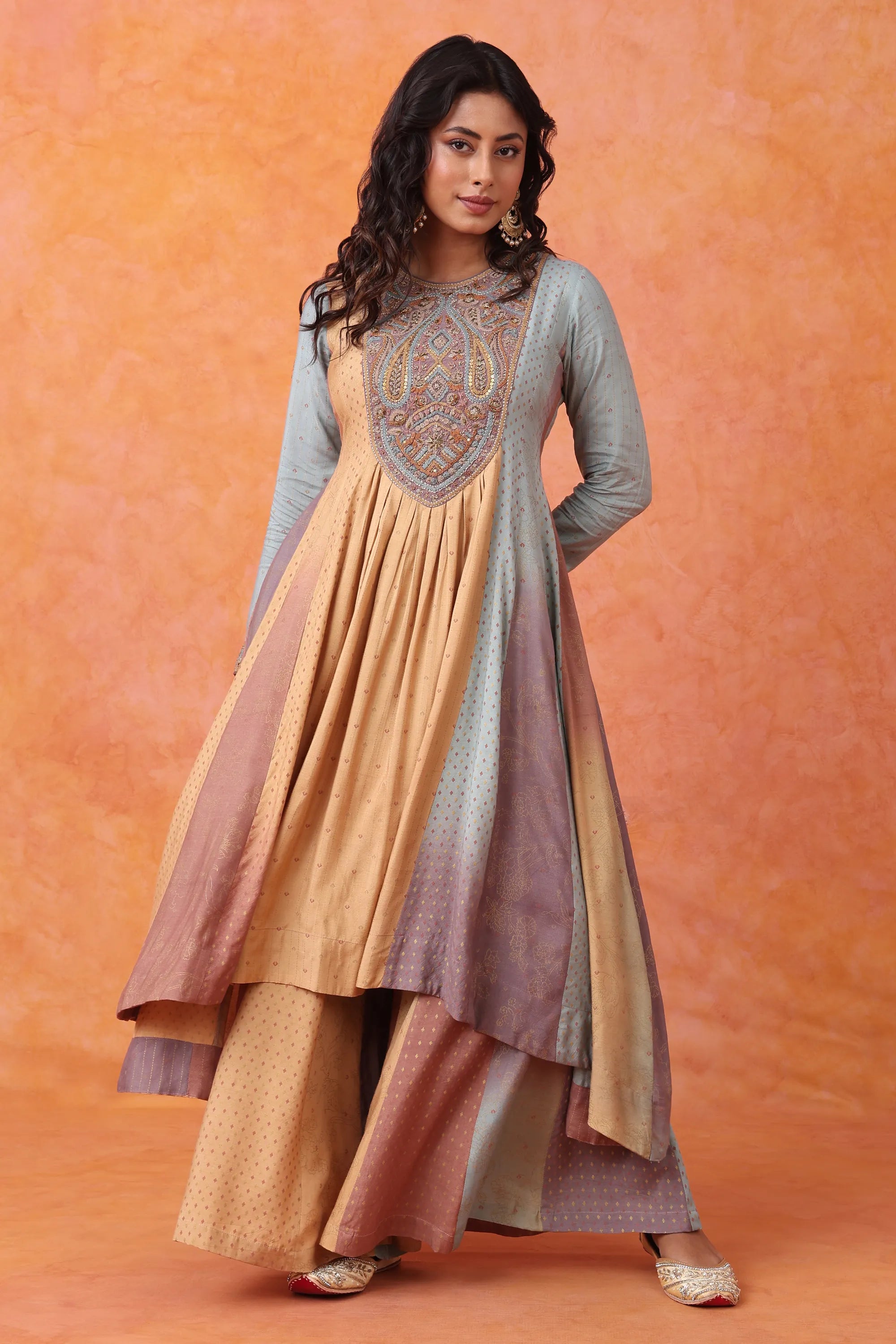 Woman wearing a traditional outfit with a long dress and matching shawl against an orange background