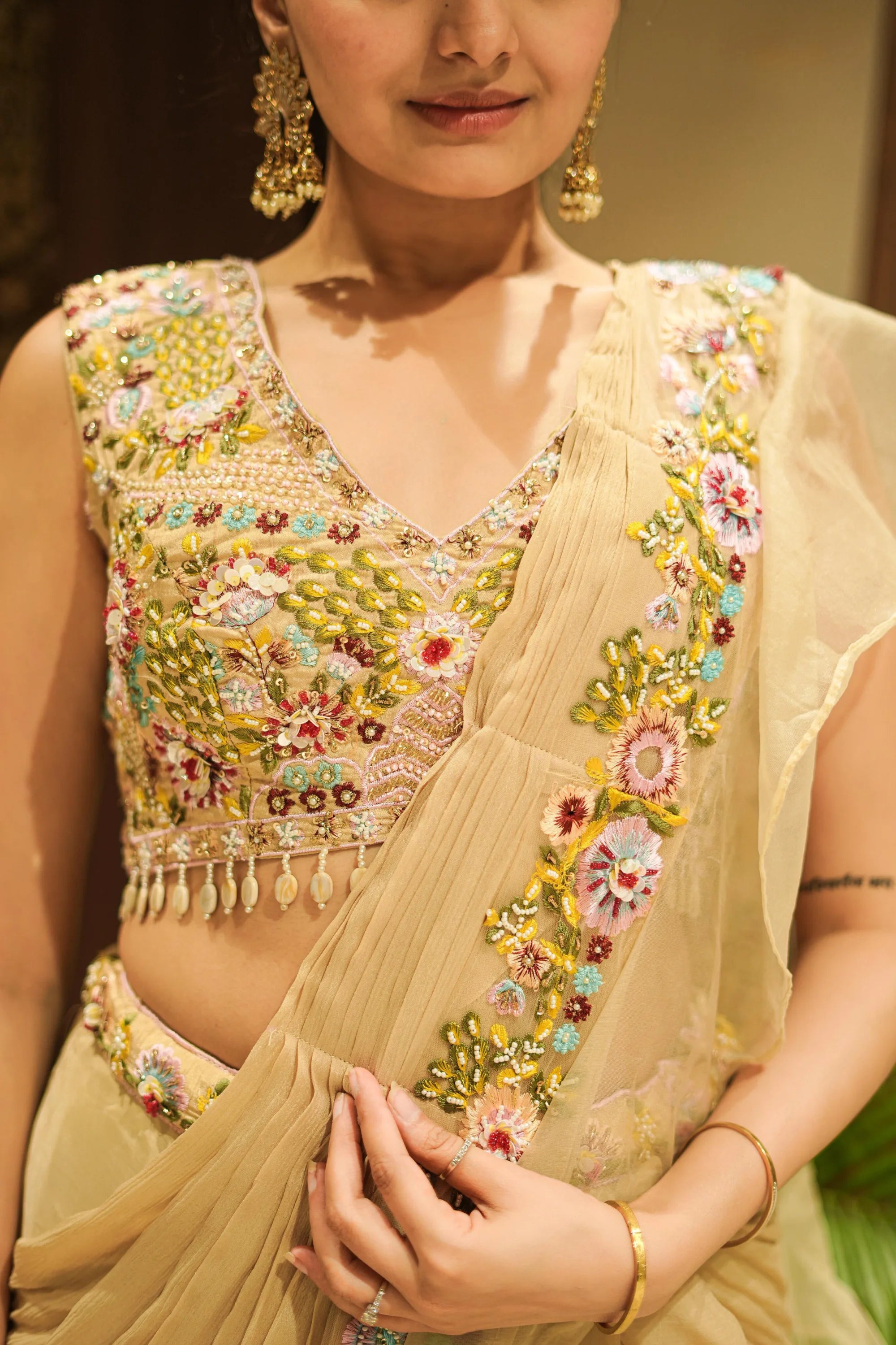 Woman wearing a beige saree with floral embroidery and gold jewelry.