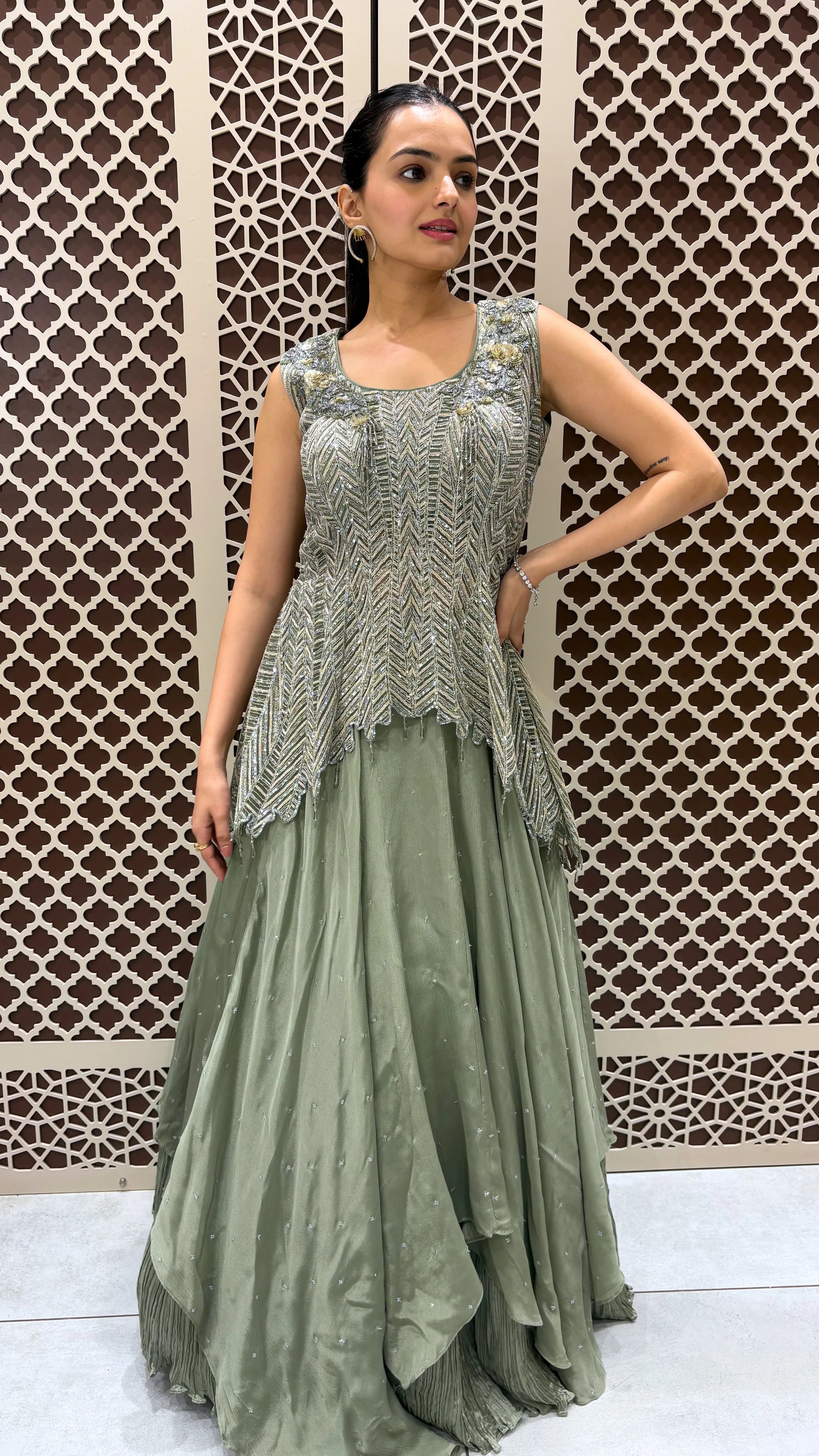 Woman wearing a green traditional outfit with intricate detailing against a decorative wall.