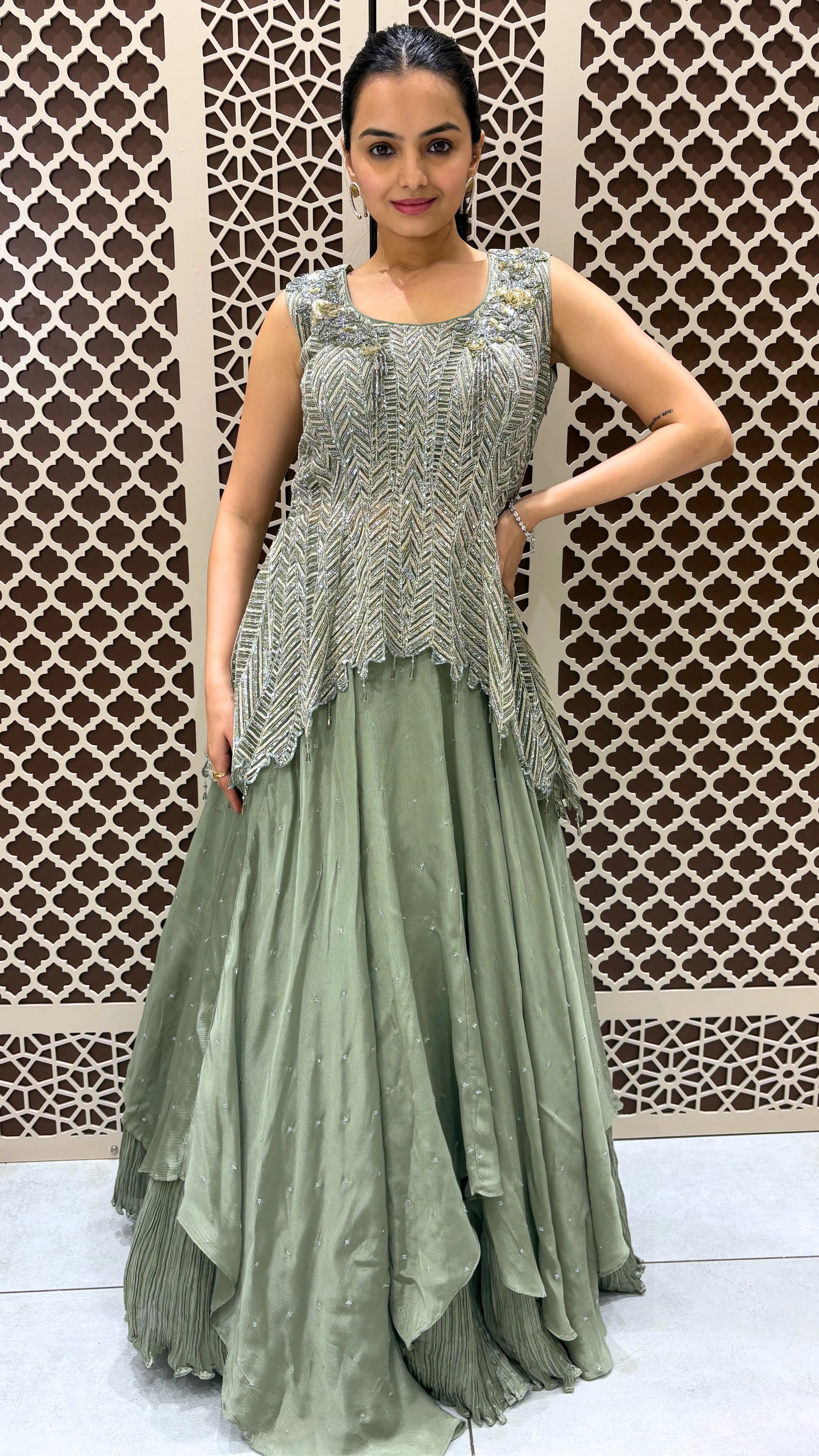 Woman wearing a green and silver traditional outfit against a decorative wall.