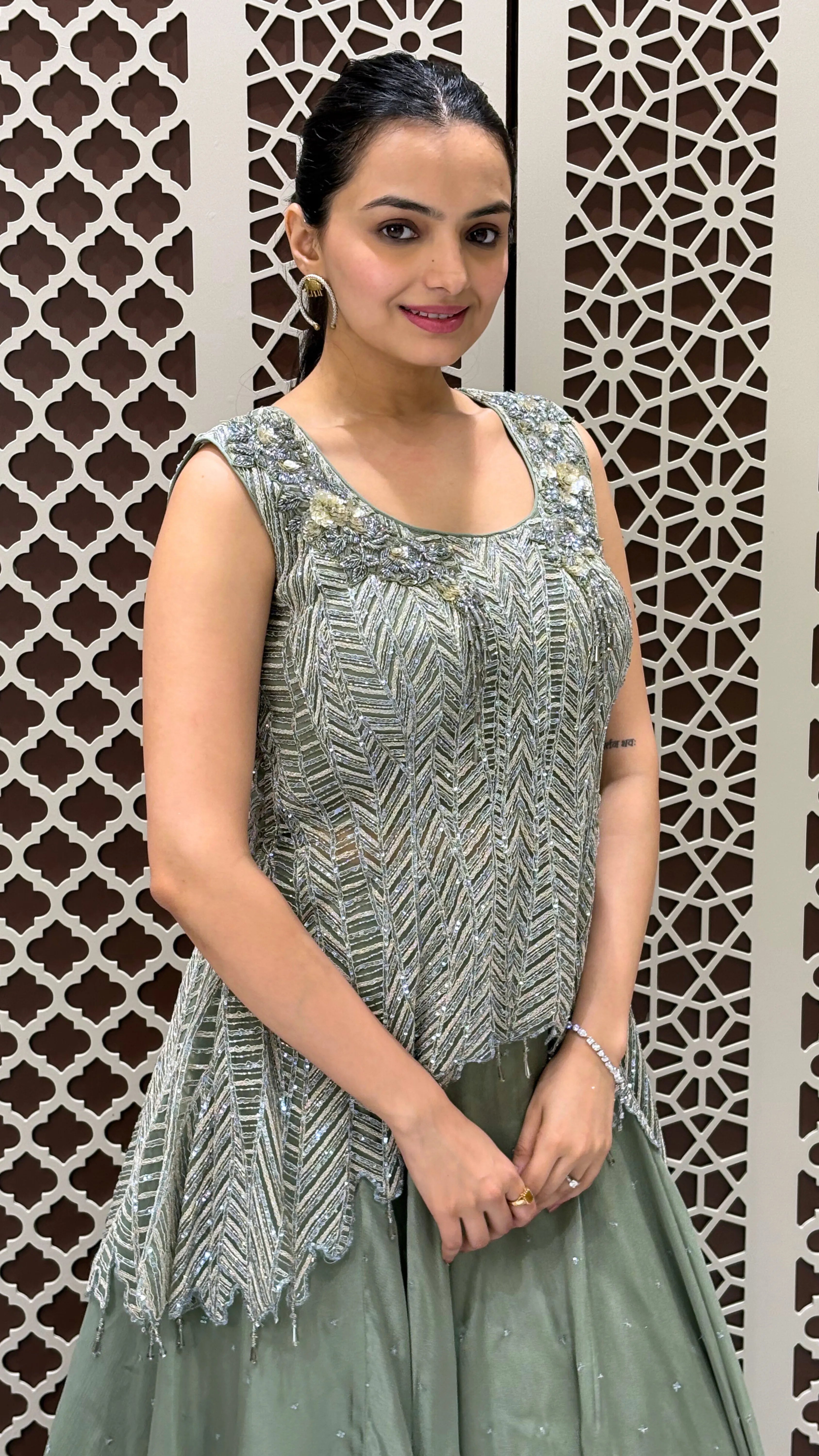 Woman wearing a green embroidered top and skirt against a decorative wall.