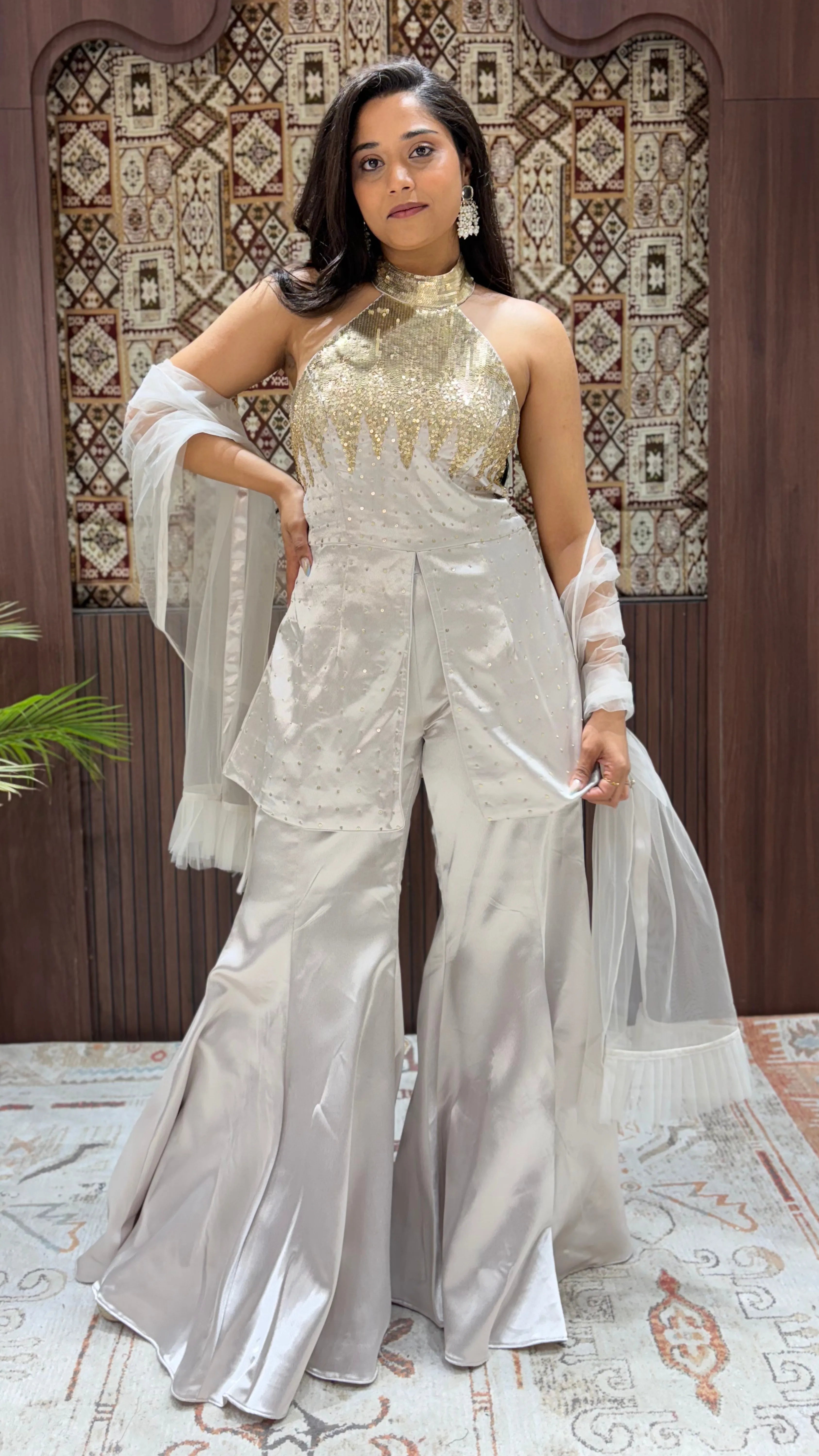 Woman in a silver outfit with a patterned wall and rug in the background