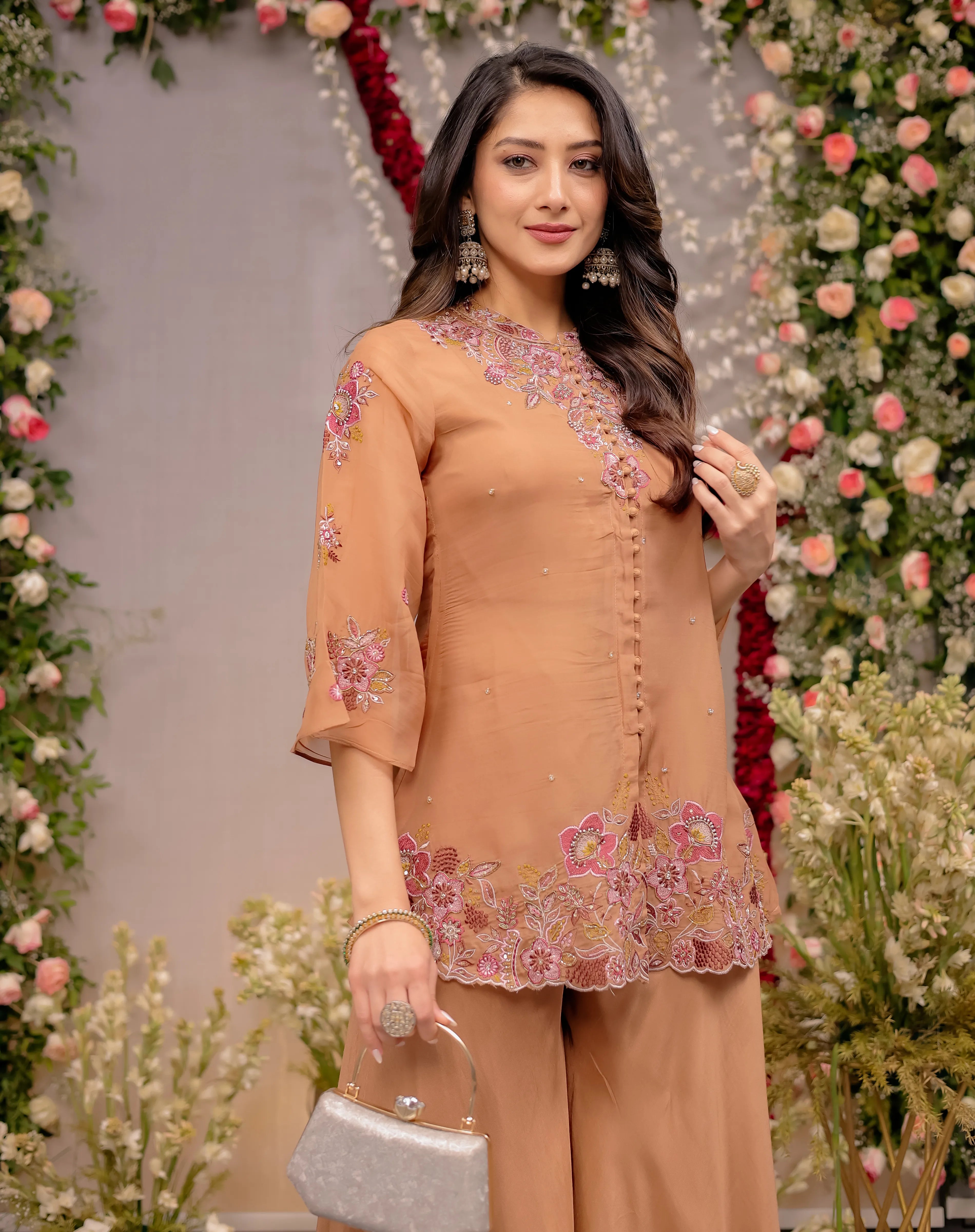 Woman in a peach embroidered outfit standing in front of floral decorations