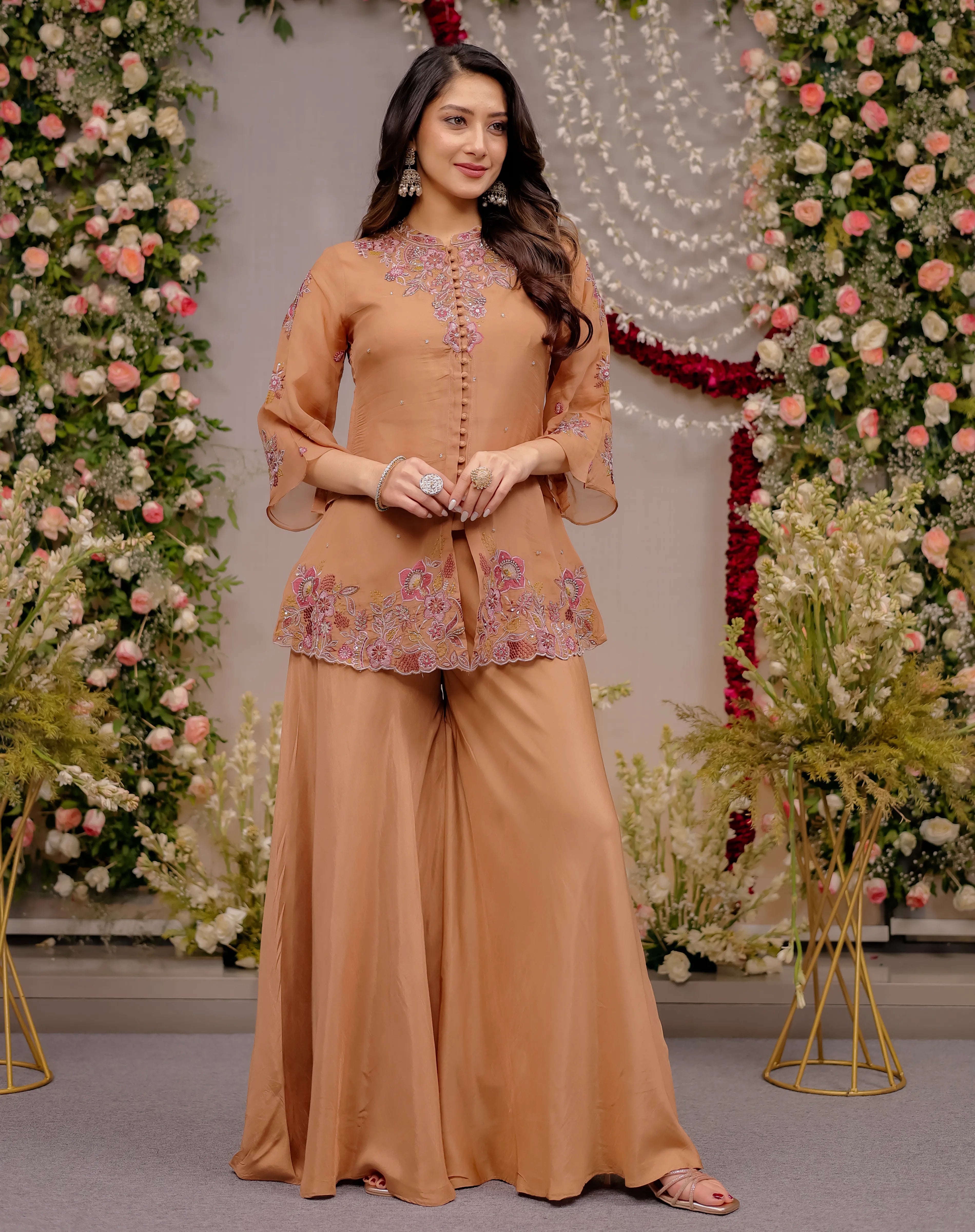Woman in a peach traditional outfit standing in front of floral decorations