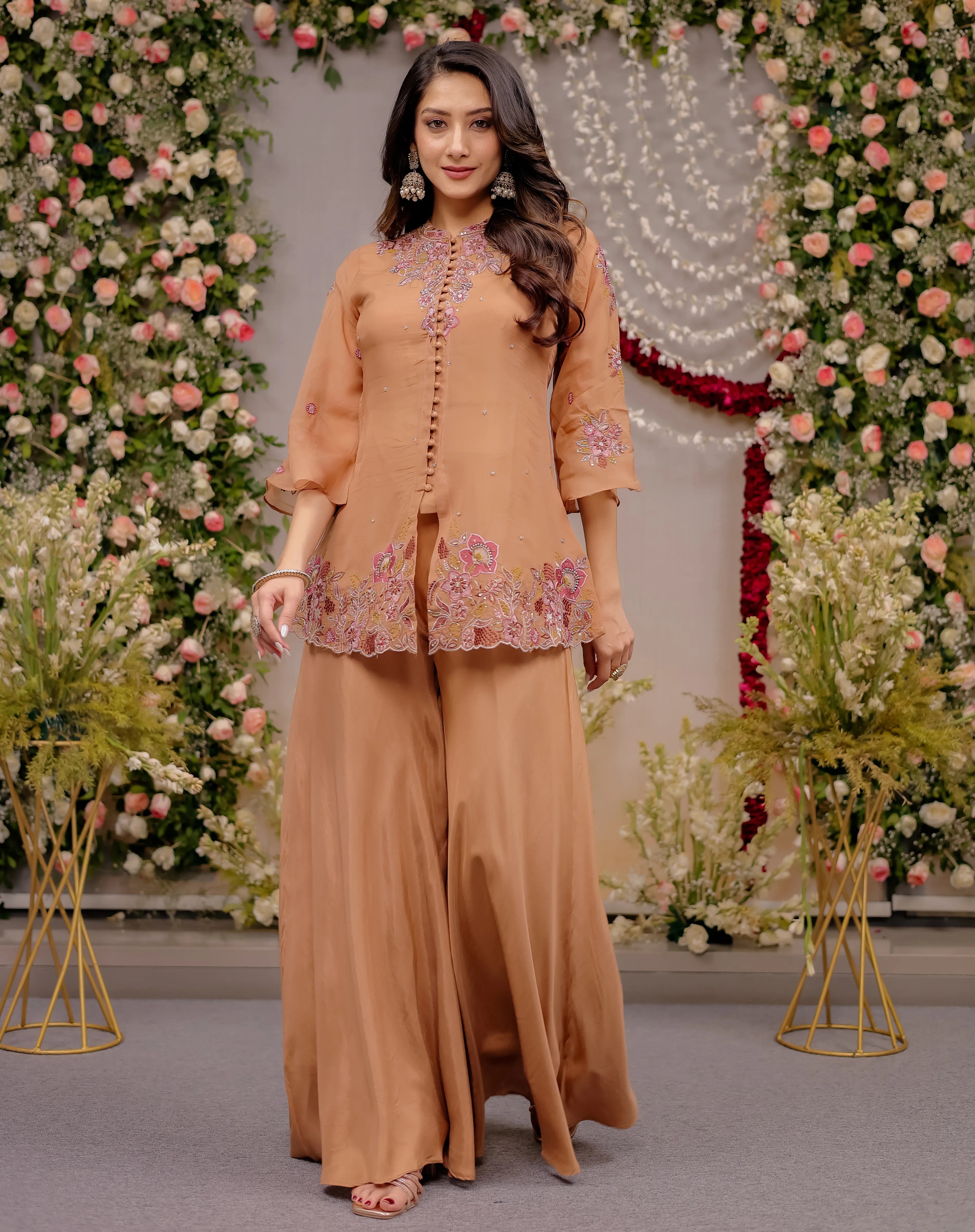 Woman in a peach traditional outfit standing in front of floral decorations