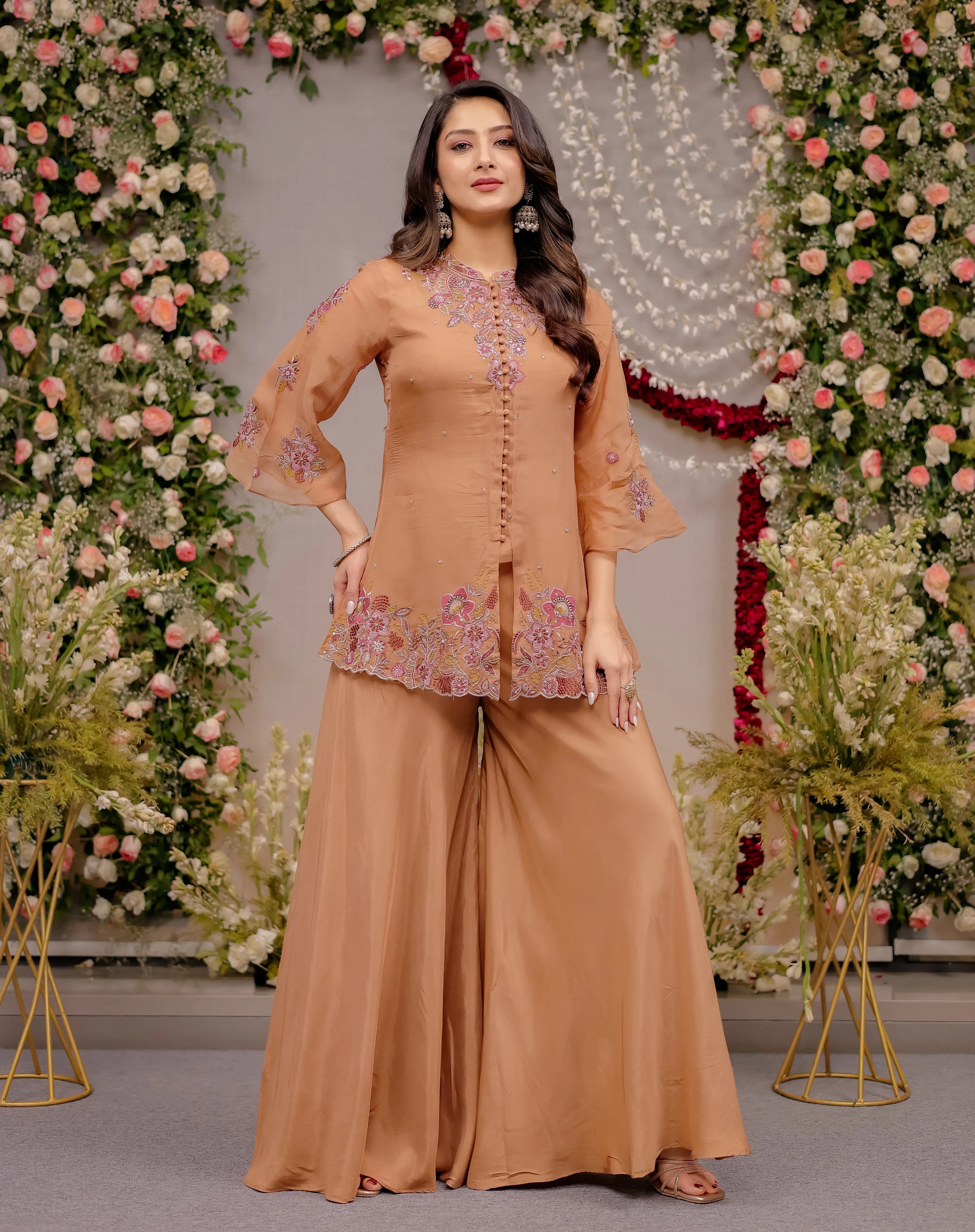 Woman in a peach embroidered outfit standing in front of floral decorations