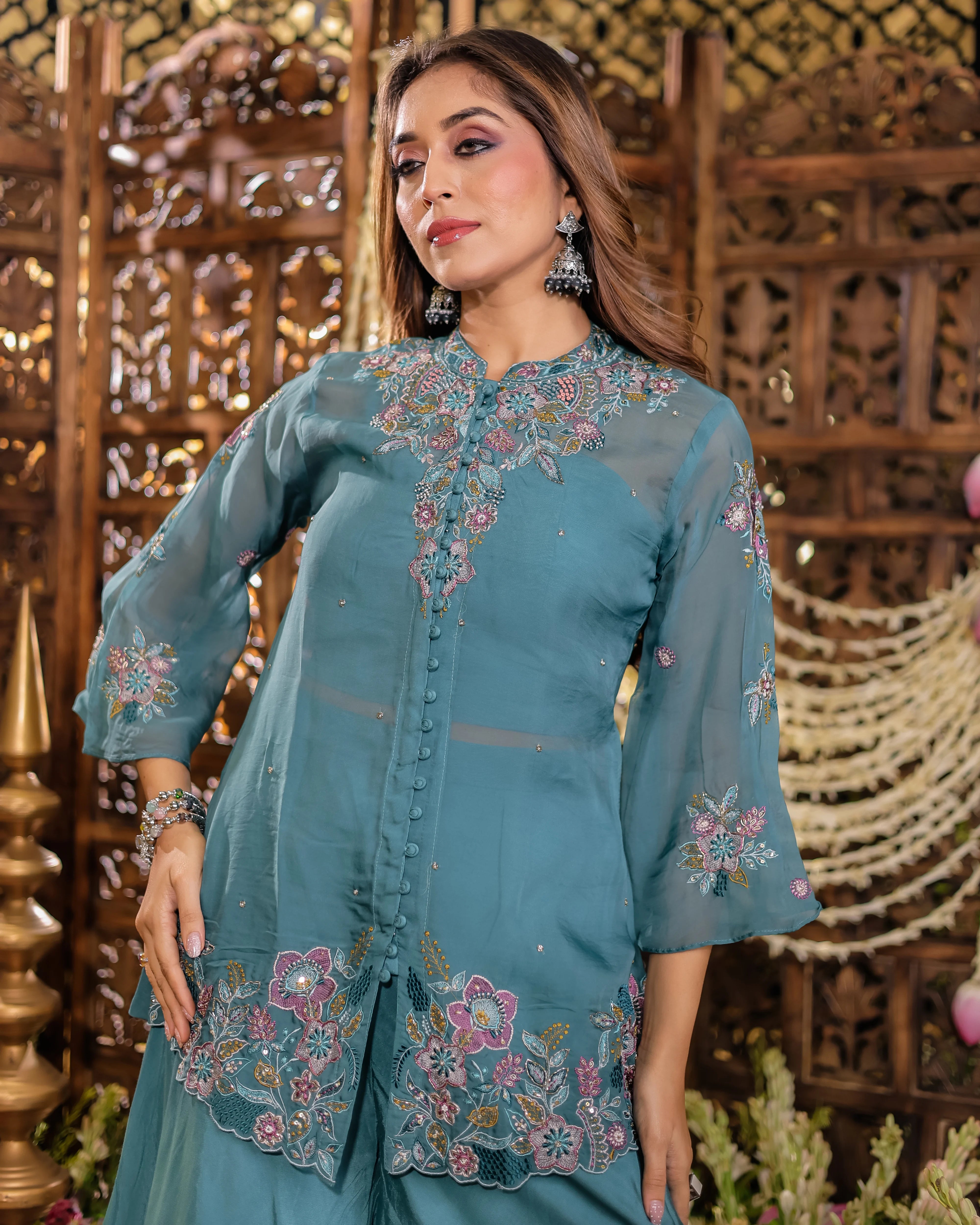 Woman wearing a teal embroidered outfit with a decorative background