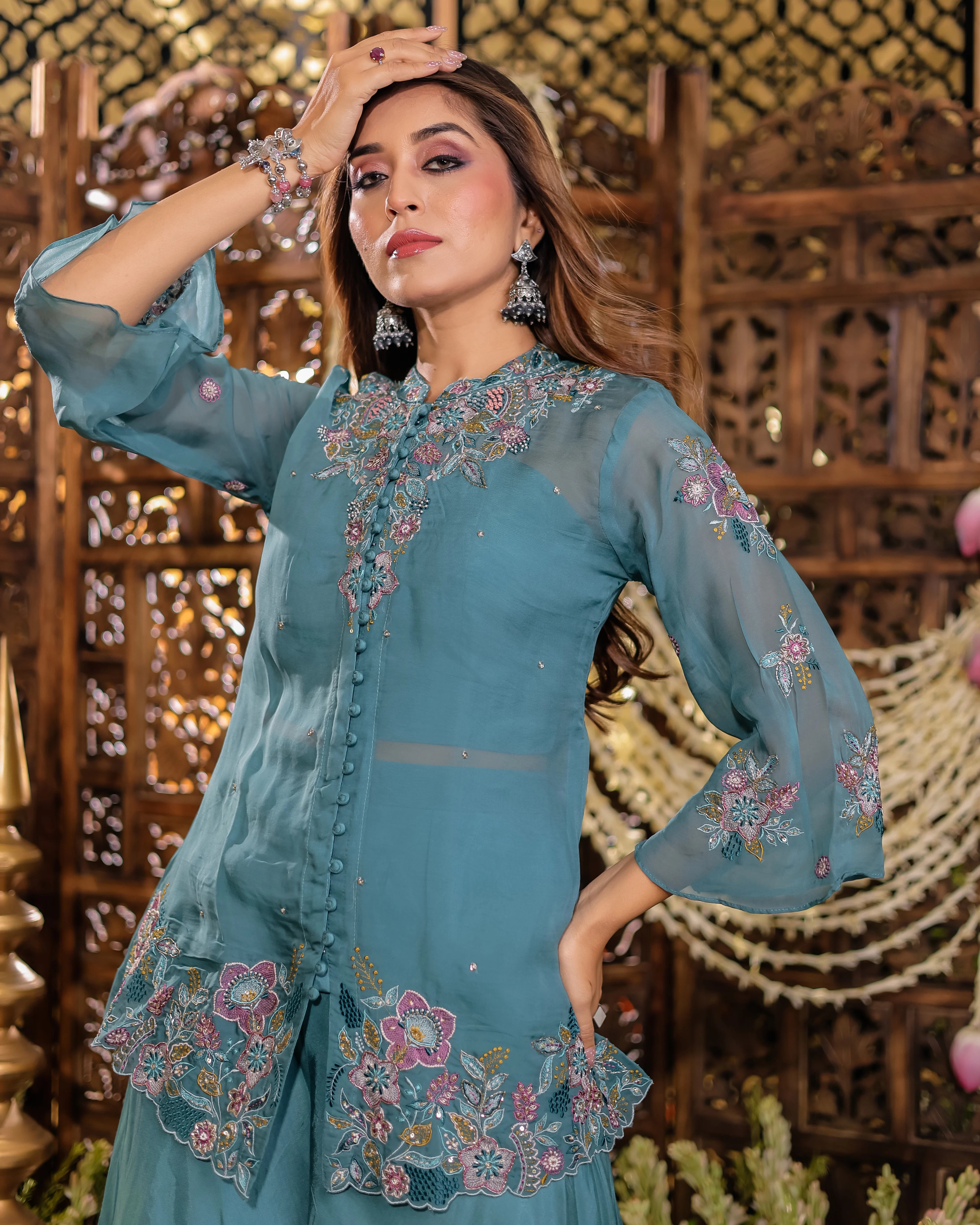 Woman wearing a teal embroidered outfit with a decorative background