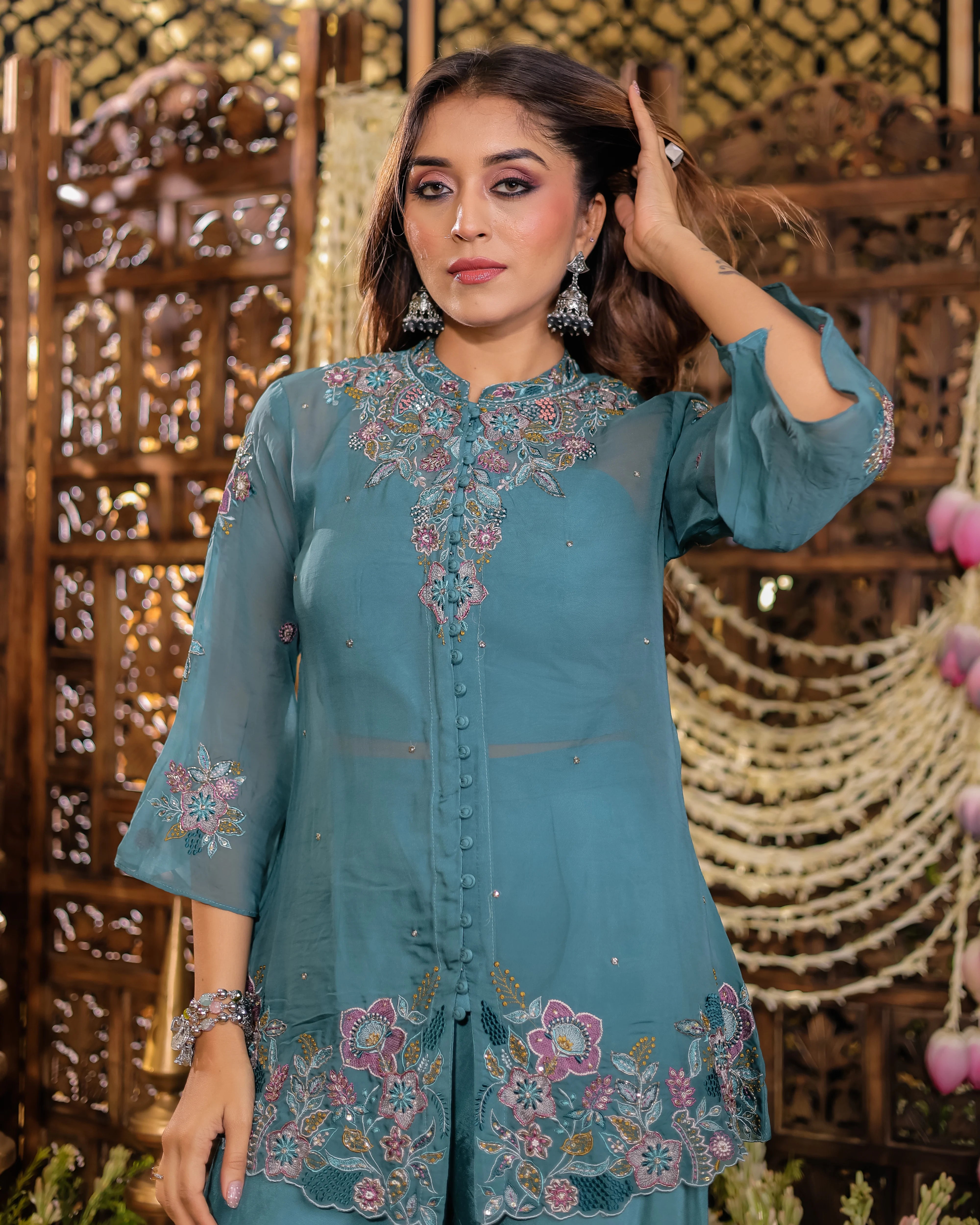 Woman wearing a teal embroidered outfit against a decorative wooden background