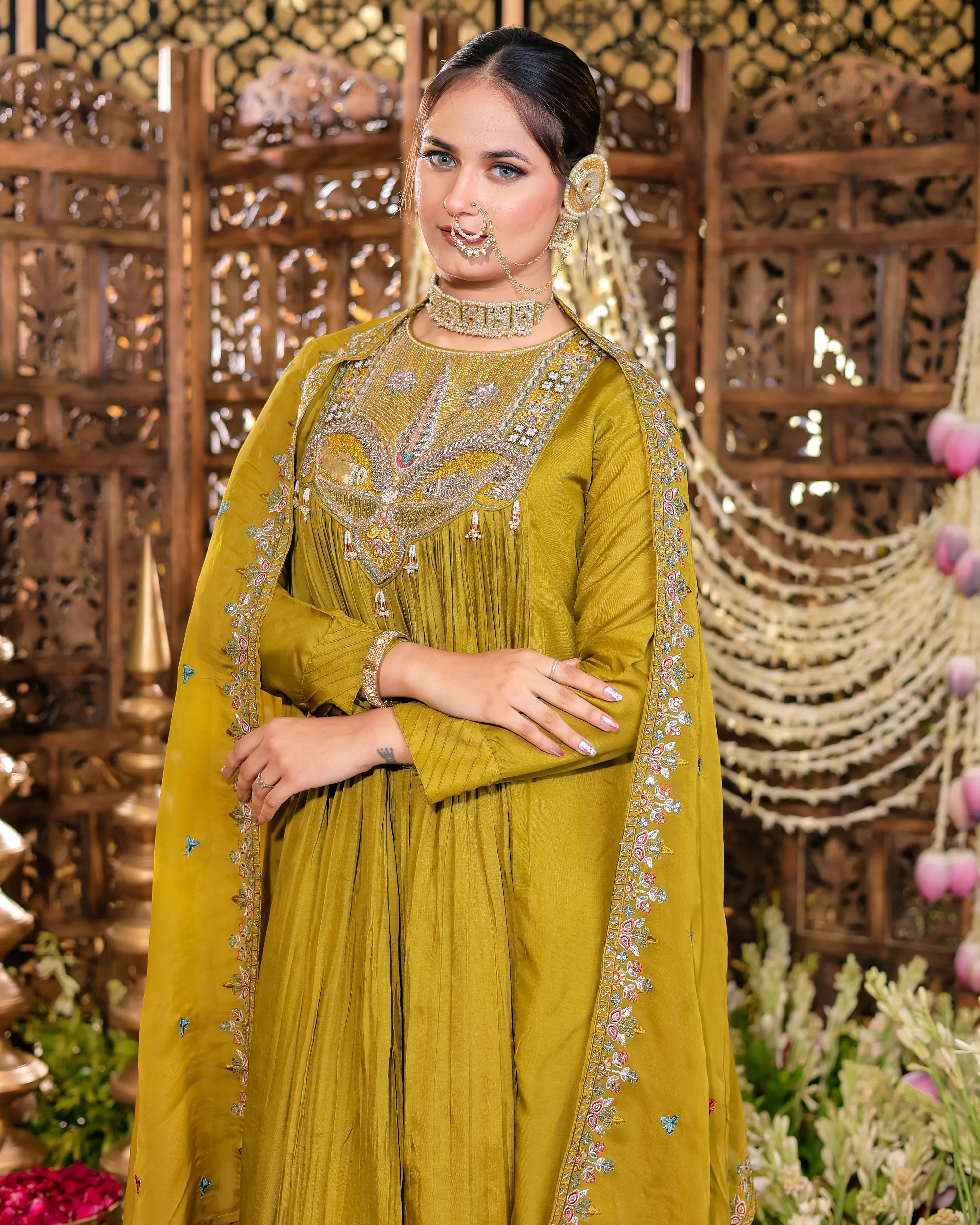 Woman in a green traditional outfit with intricate embroidery against a decorative background
