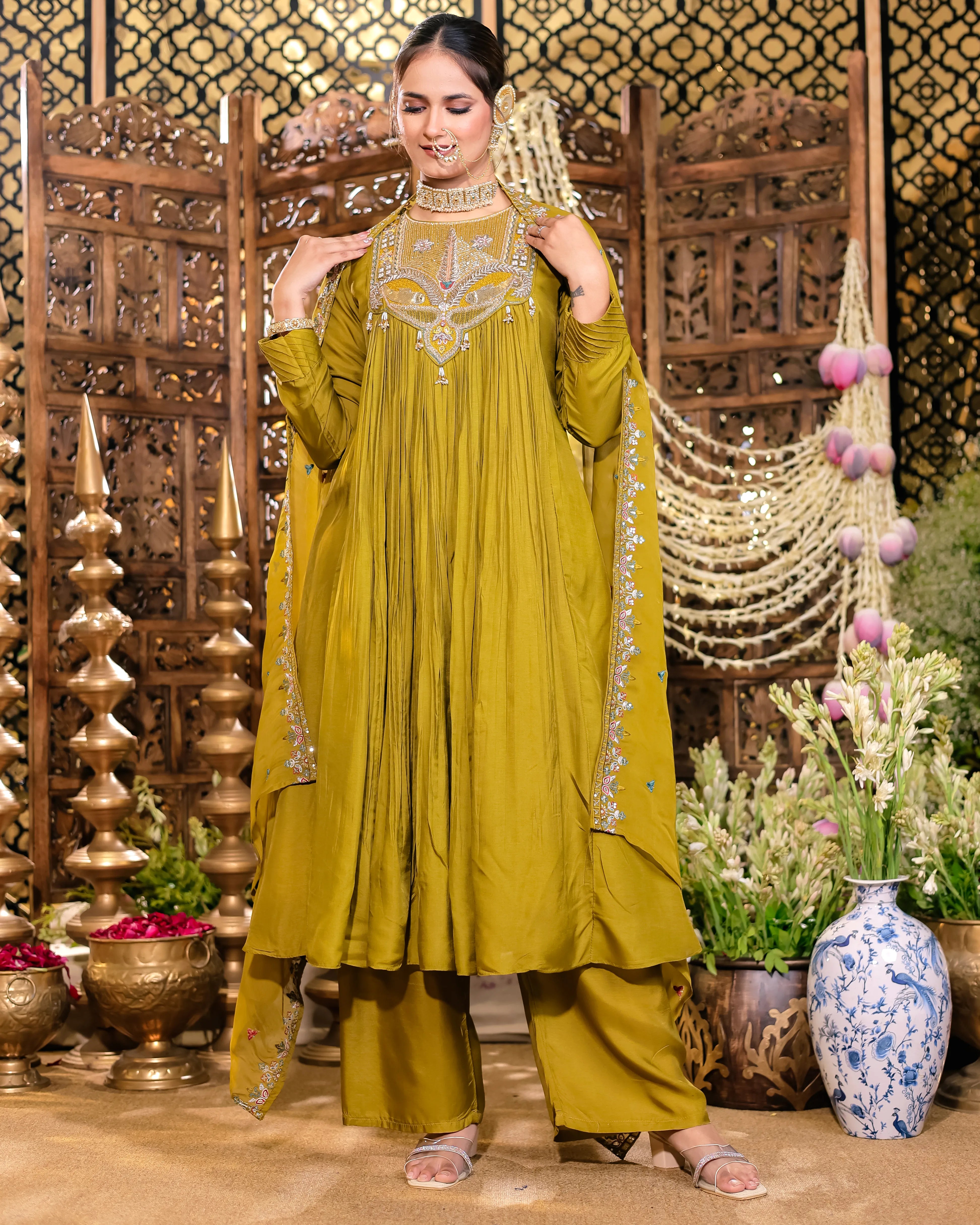Woman in a green traditional outfit with intricate embroidery in a decorative setting.