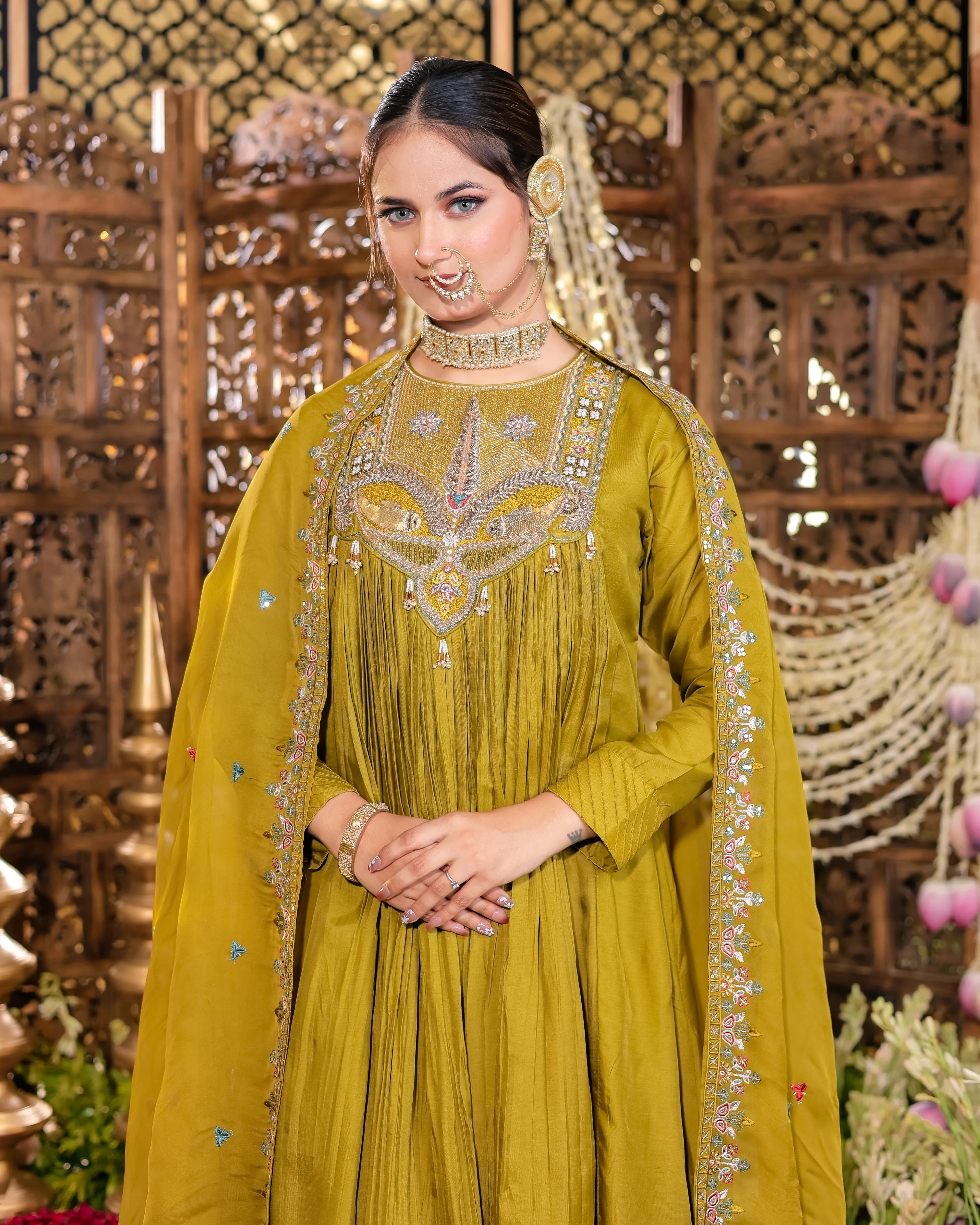 Woman in a yellow traditional outfit with intricate designs, standing against a decorative background.