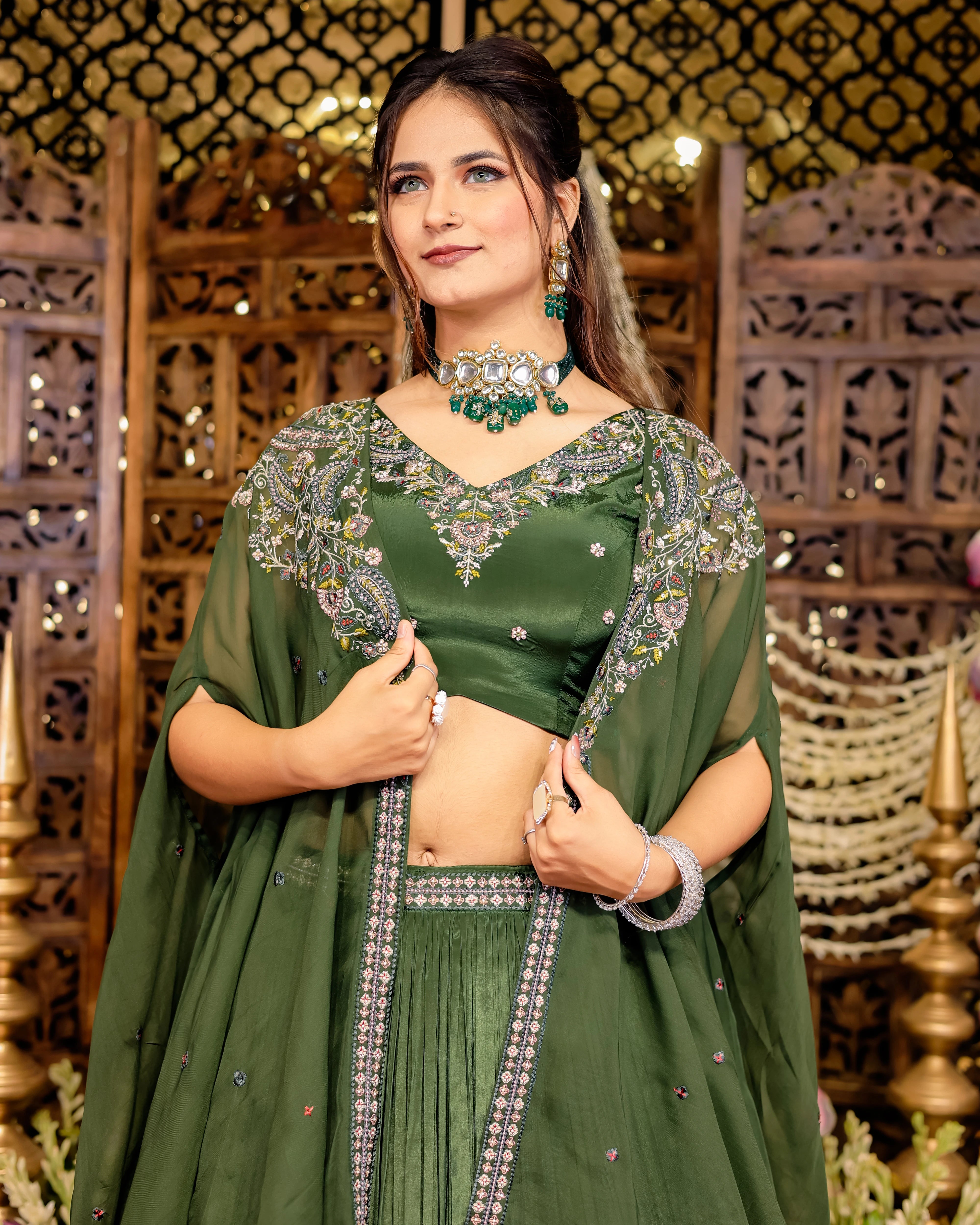 Woman wearing a dark green pleated lehenga and embroidered cape with silver sequin detailing.