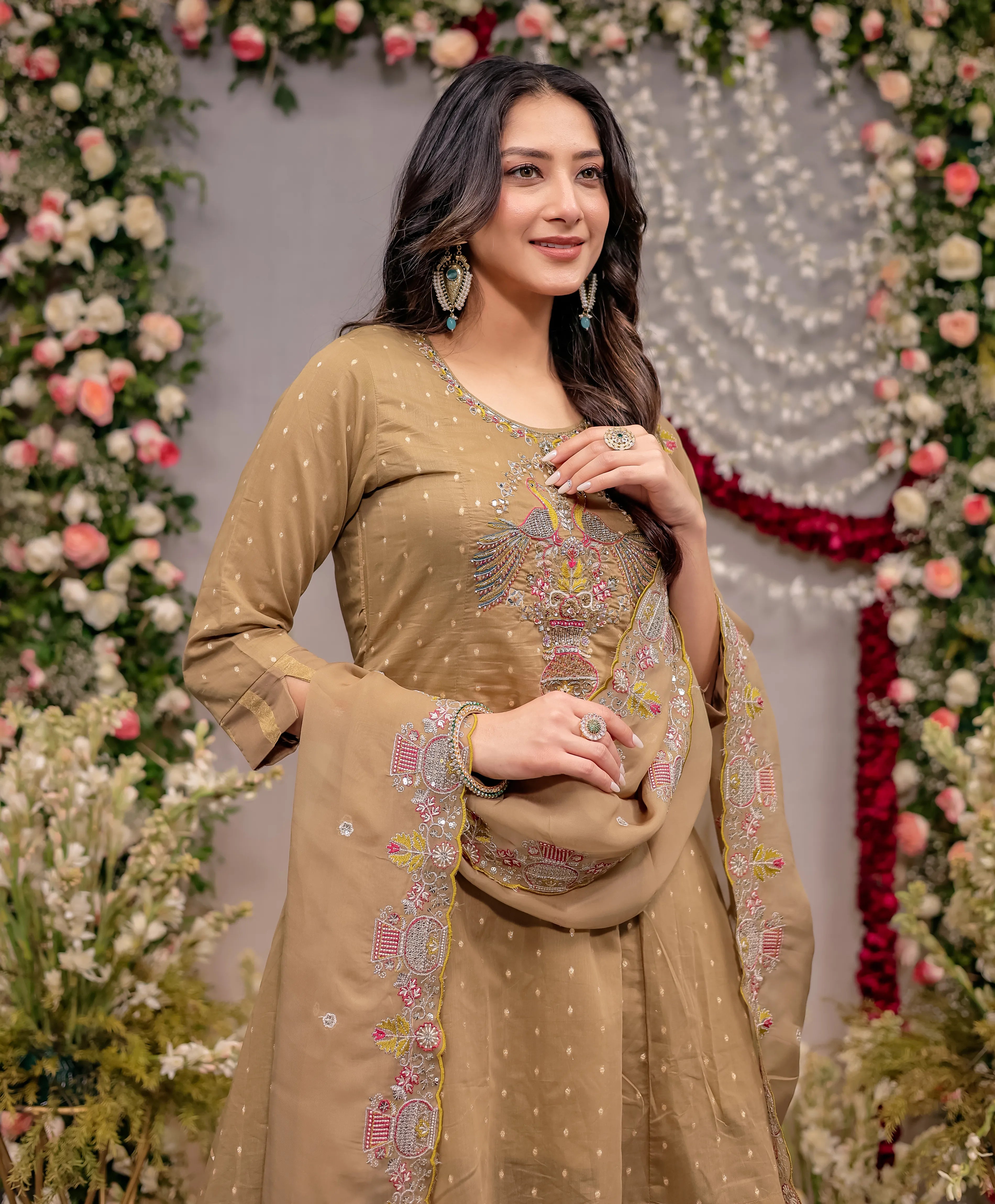 Woman in a beige embroidered traditional outfit with floral decorations in the background