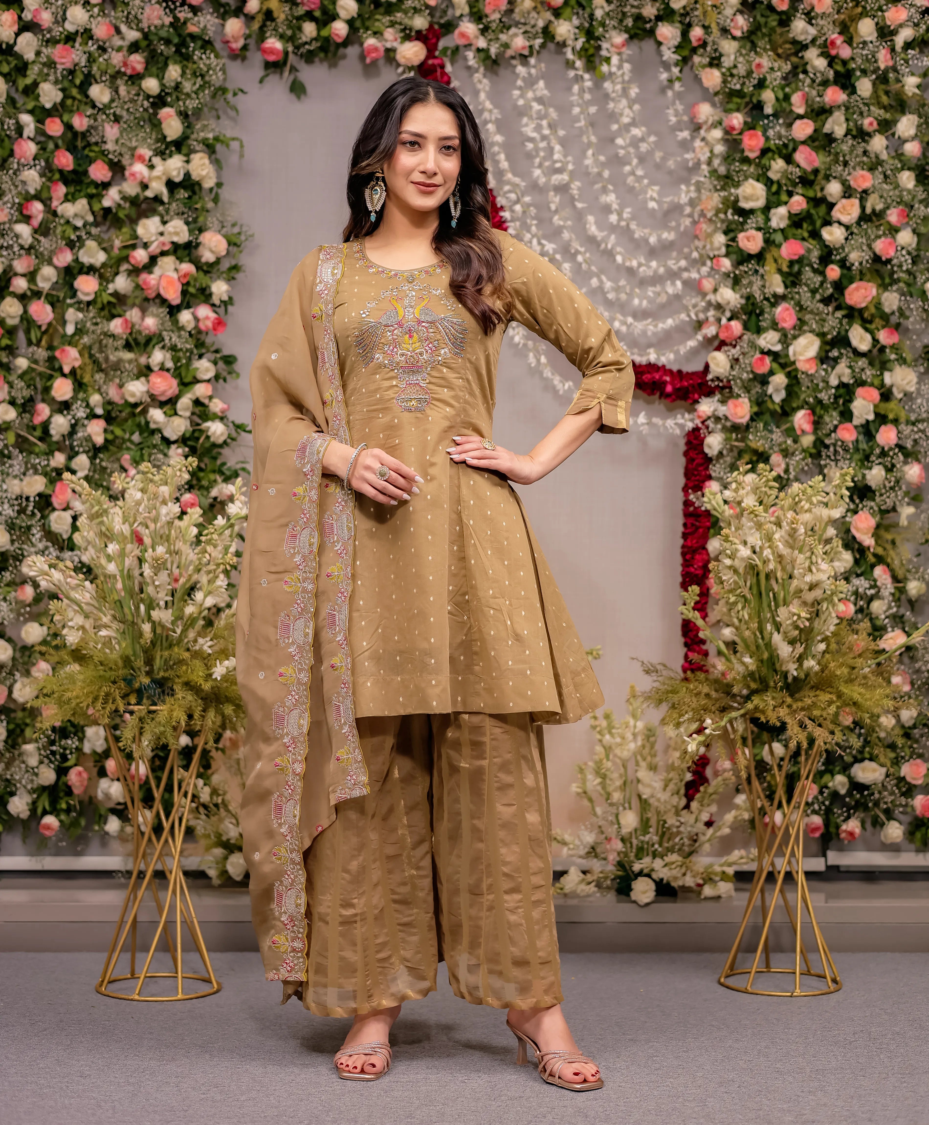 Woman in a beige traditional outfit standing in front of floral decorations