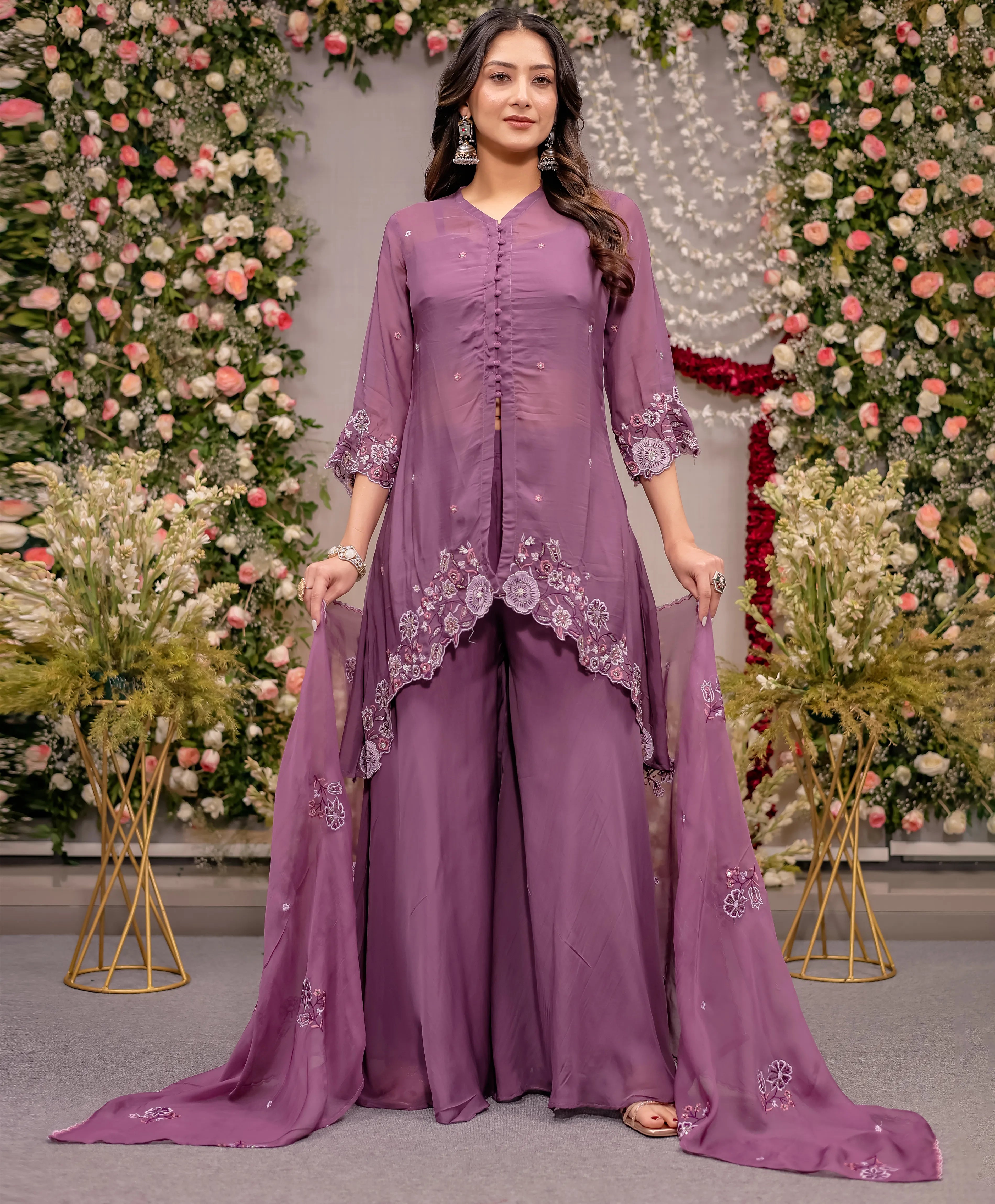 Woman in a purple traditional outfit with floral embroidery against a decorated floral backdrop