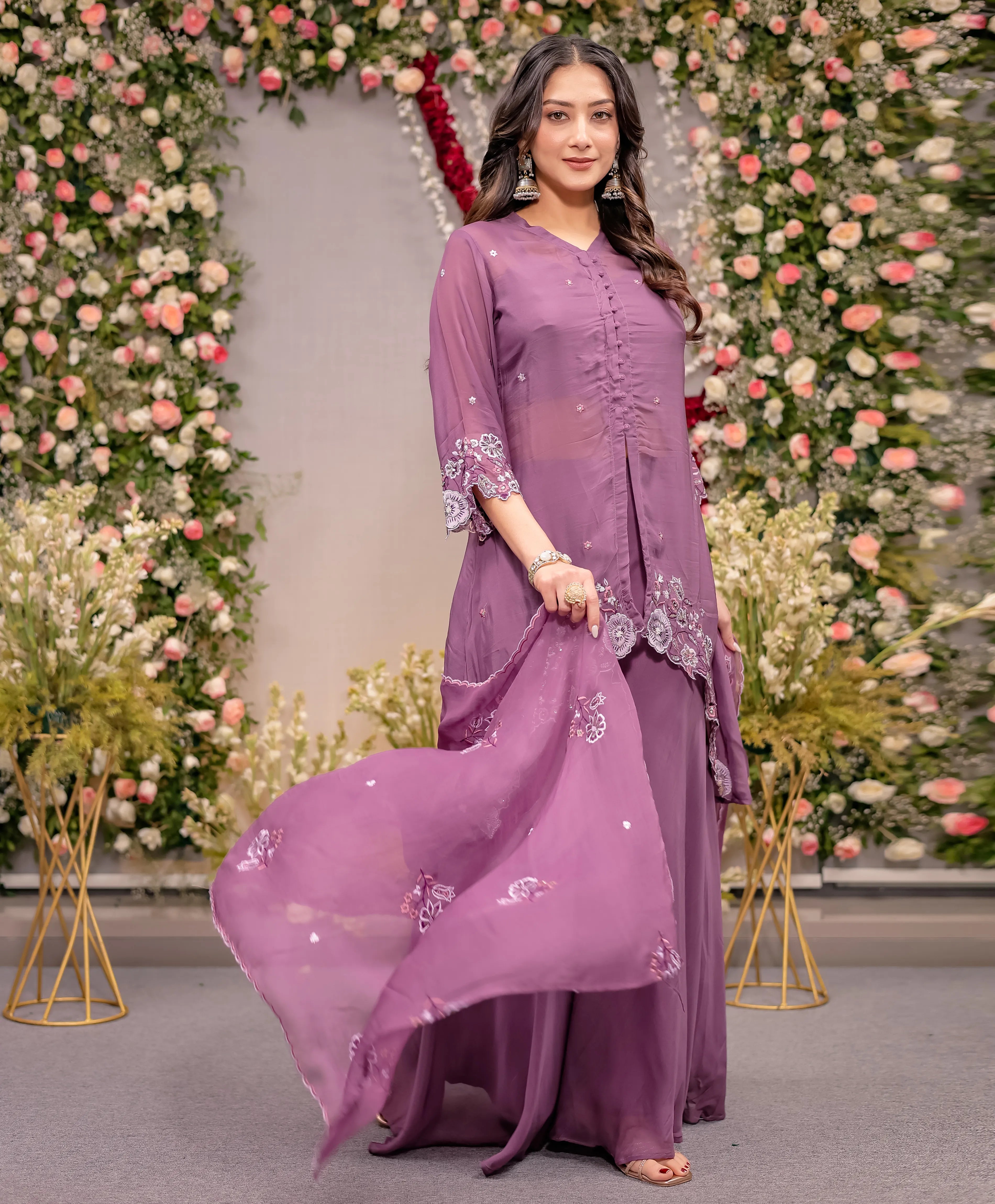 Woman in a purple traditional outfit standing in front of floral decorations