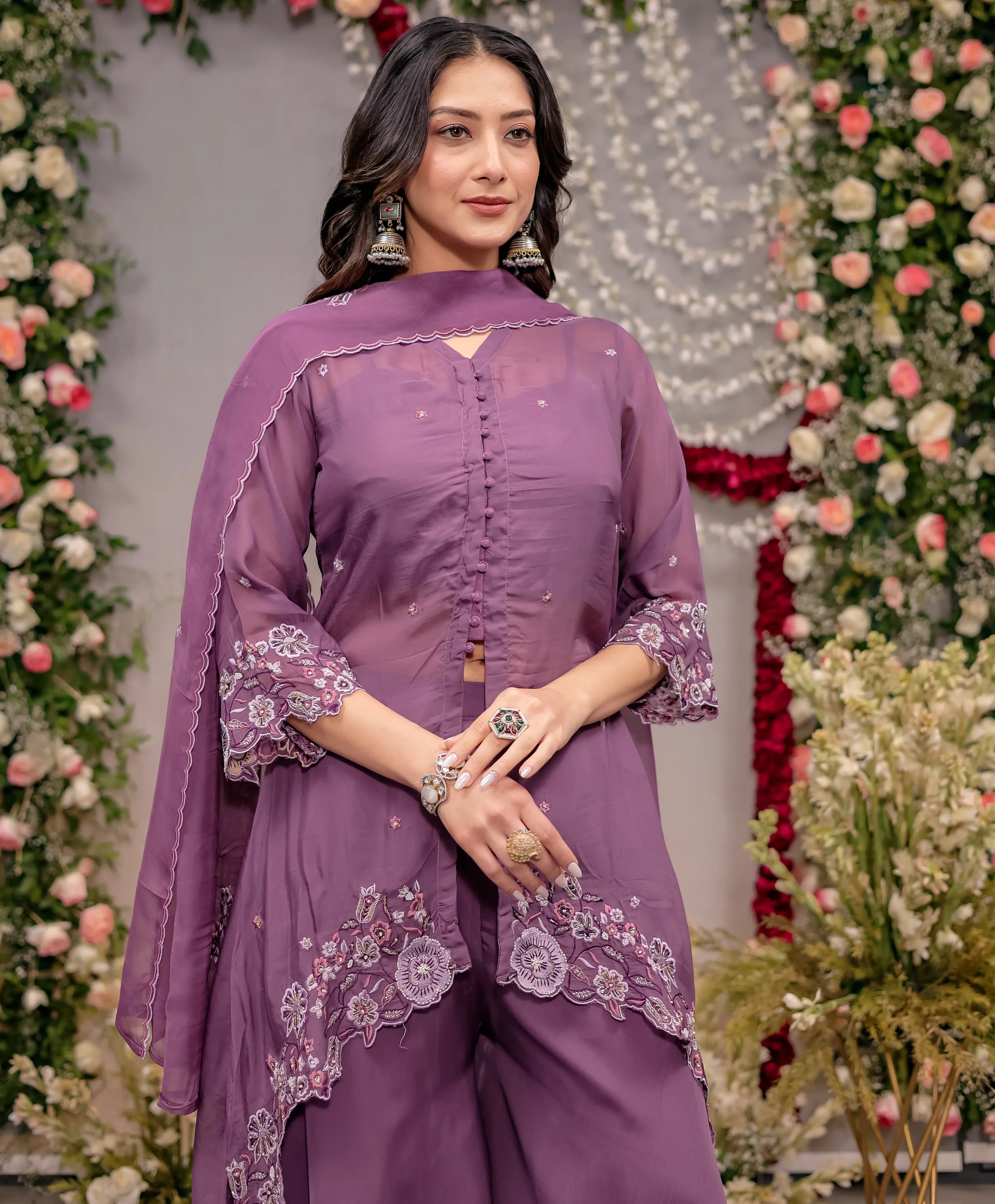 Woman in a purple traditional outfit with floral embroidery against a decorated background