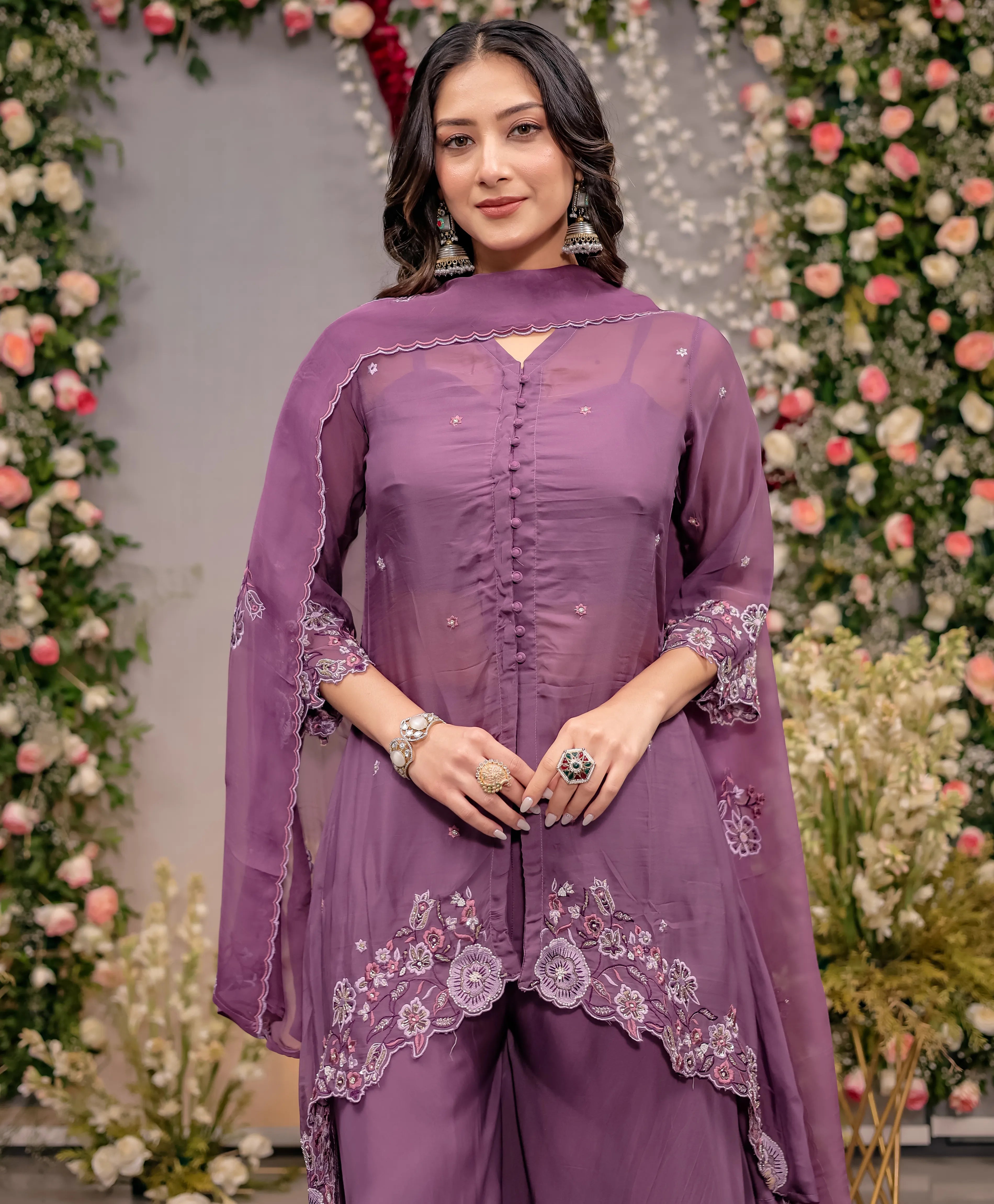Woman in a purple embroidered outfit standing in front of floral decorations