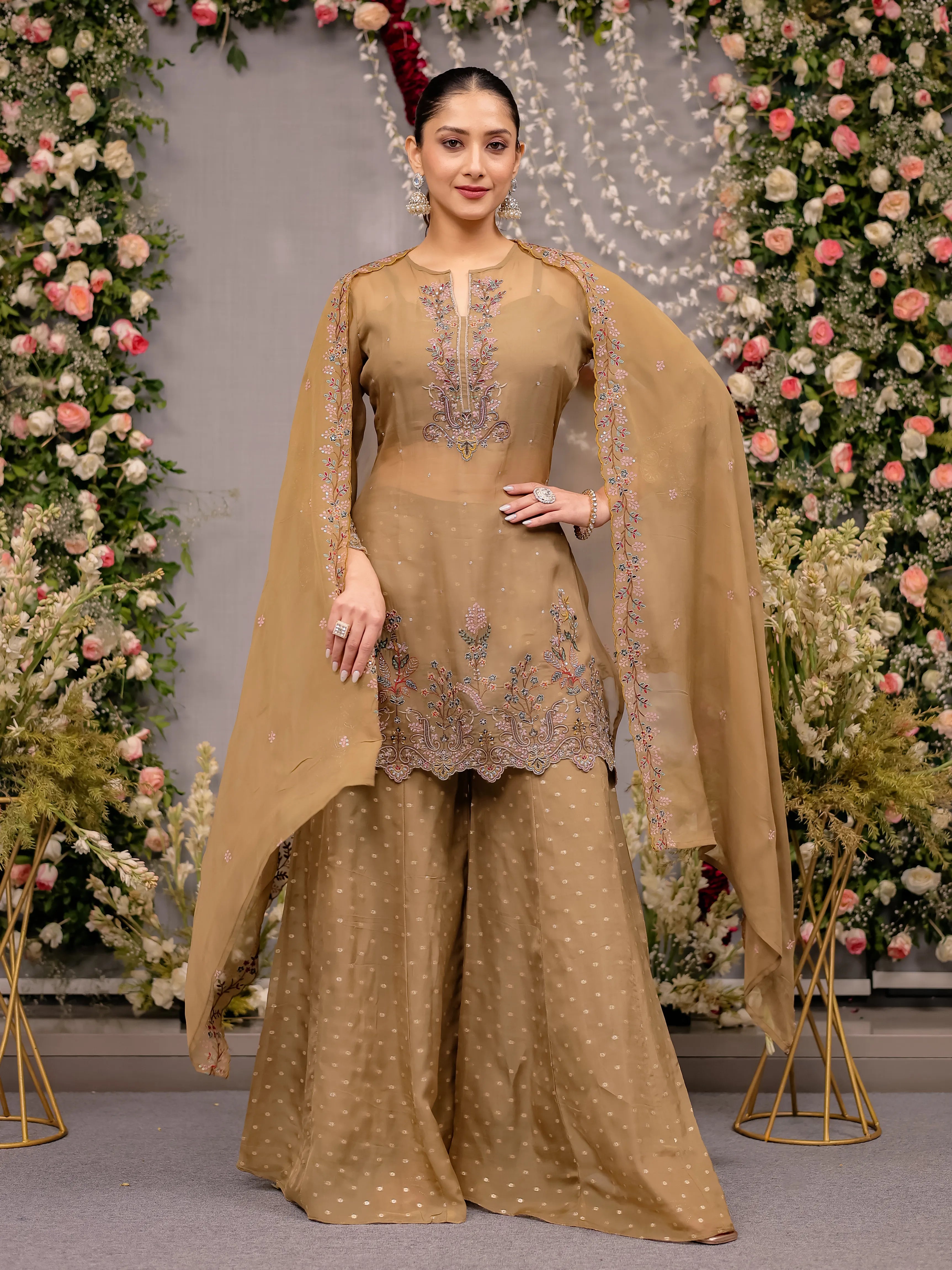 Woman in a beige traditional outfit with floral embroidery against a decorated floral backdrop
