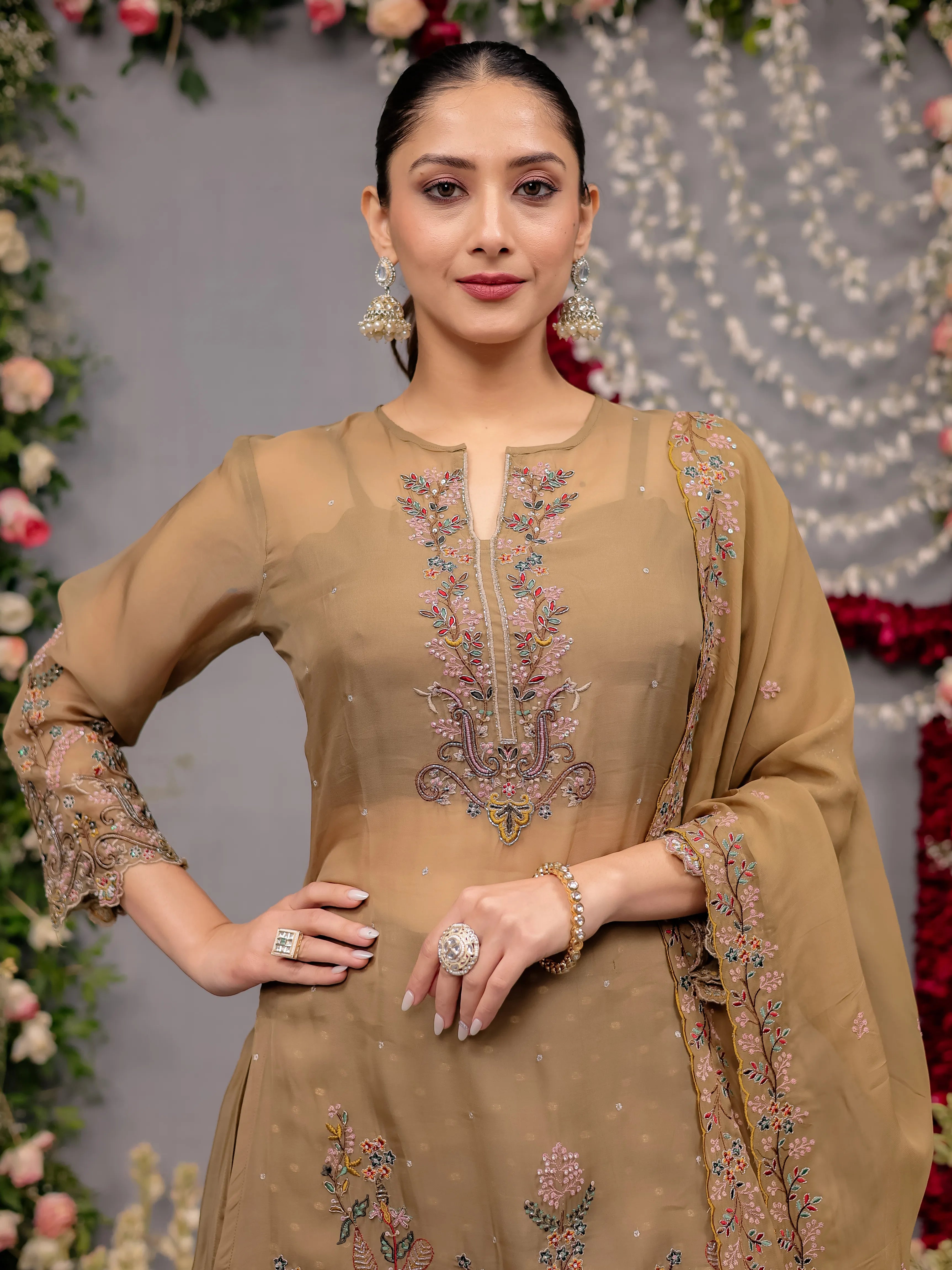 Woman in a beige embroidered traditional outfit with floral decorations in the background