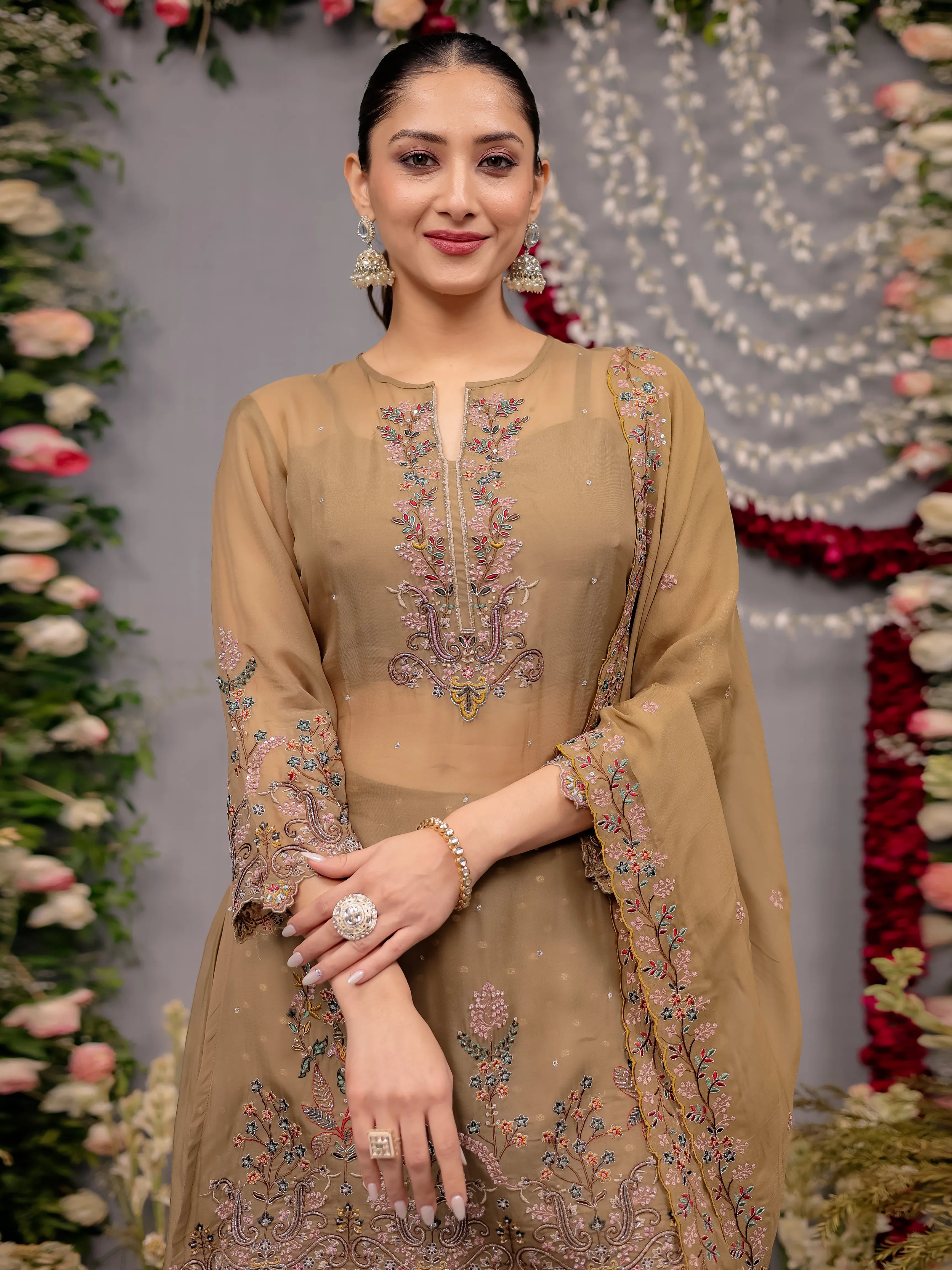 Woman in a beige embroidered traditional outfit with floral decorations in the background