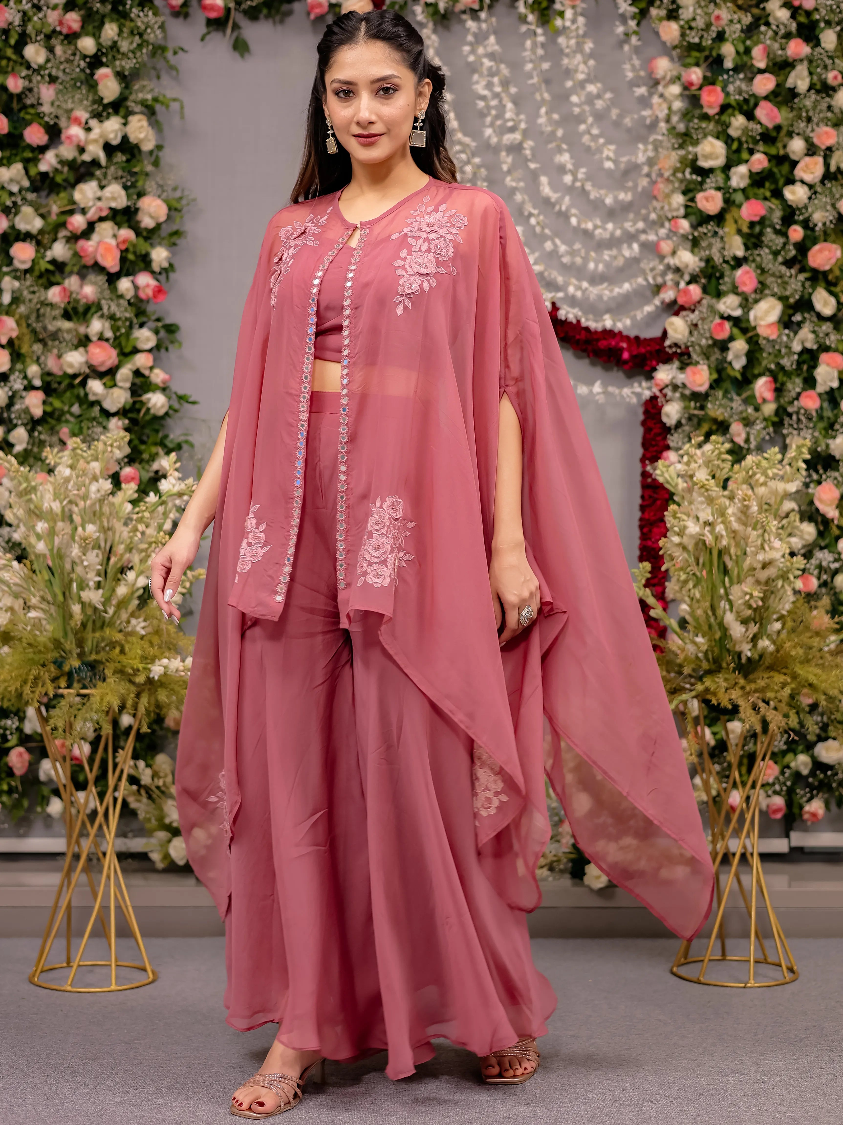 Woman in a pink traditional outfit with floral embroidery against a decorated background