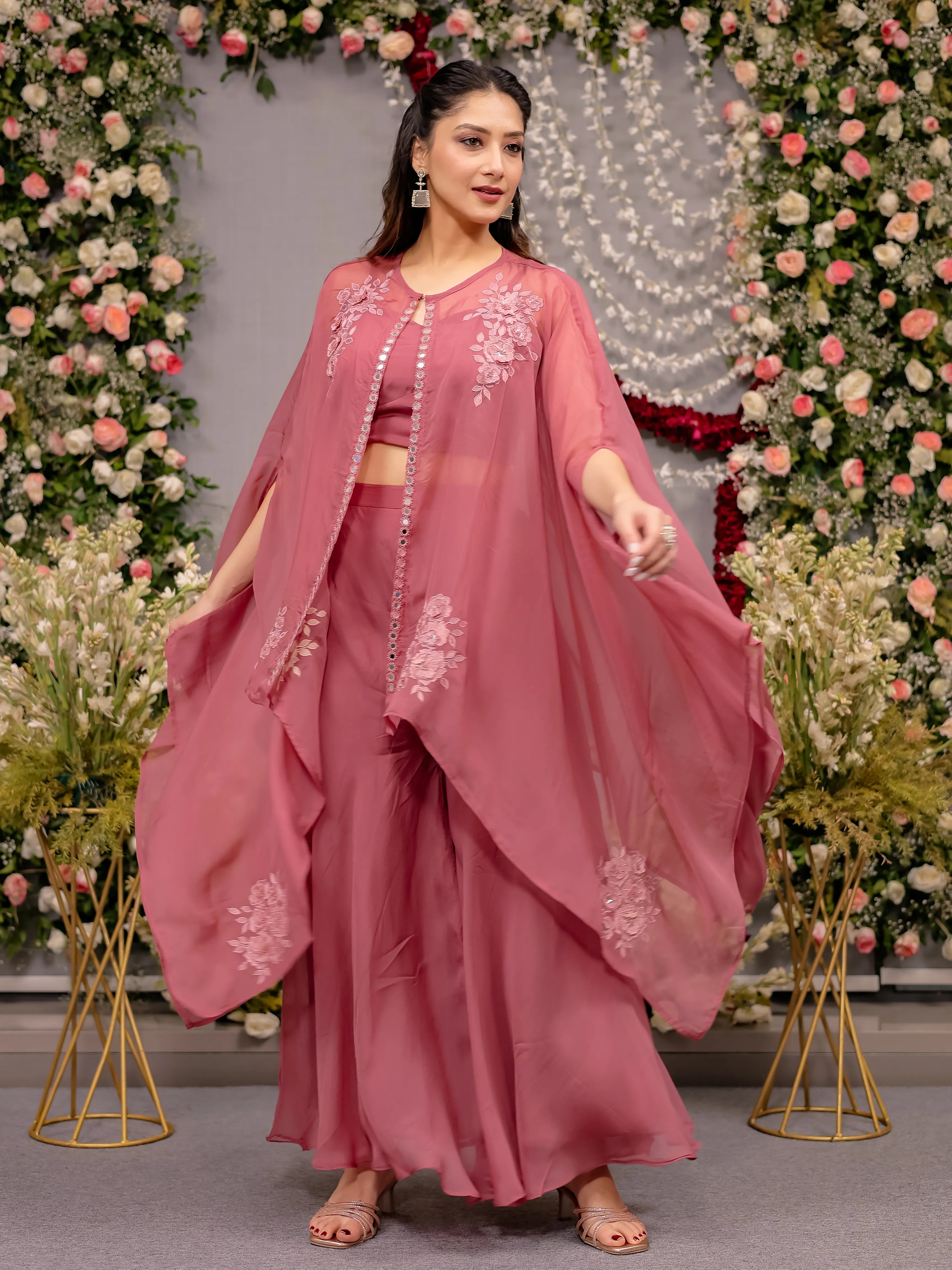 Woman in a pink traditional outfit with floral embroidery against a decorated floral backdrop