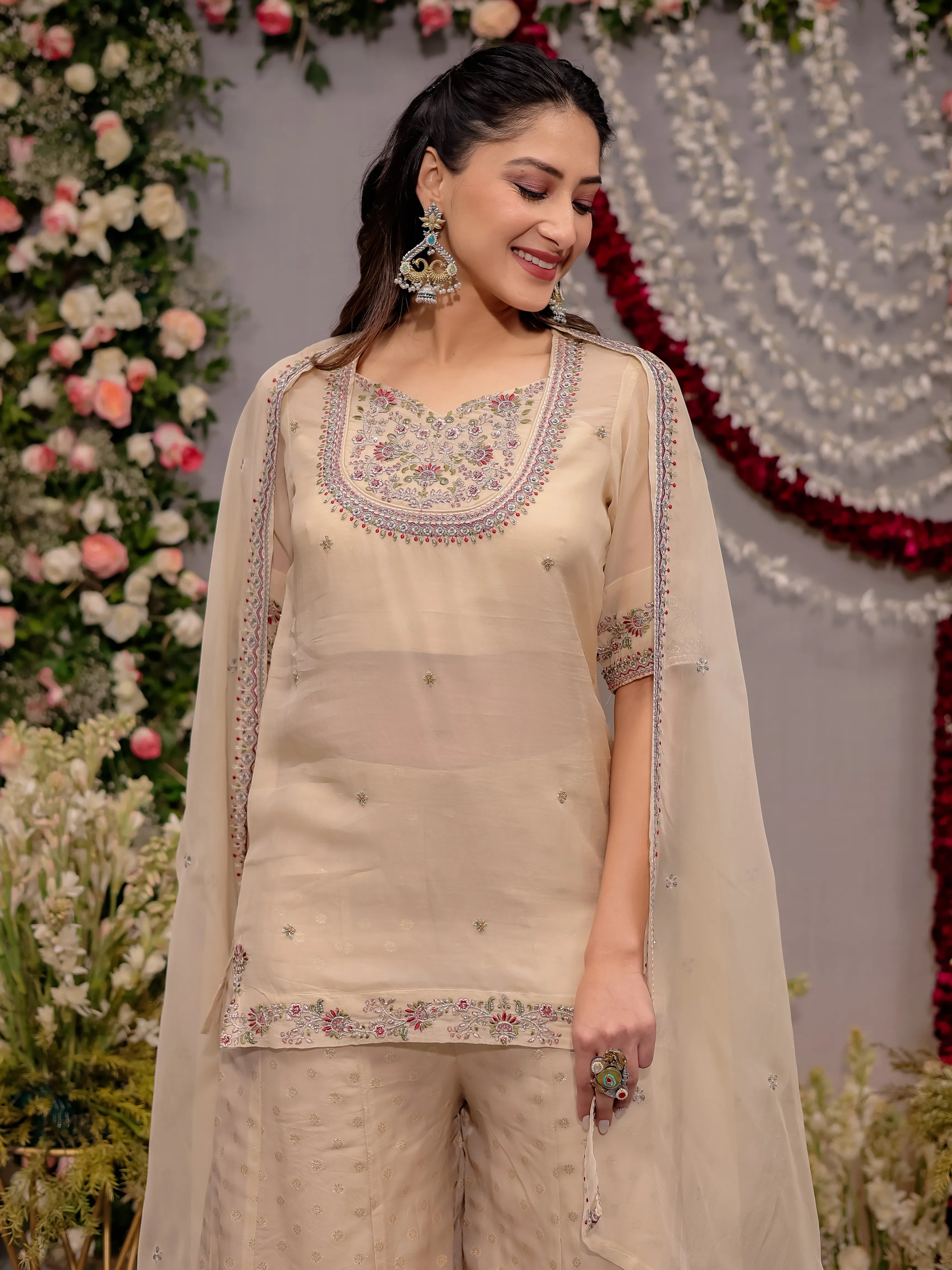 Woman in a beige embroidered outfit standing in front of floral decorations