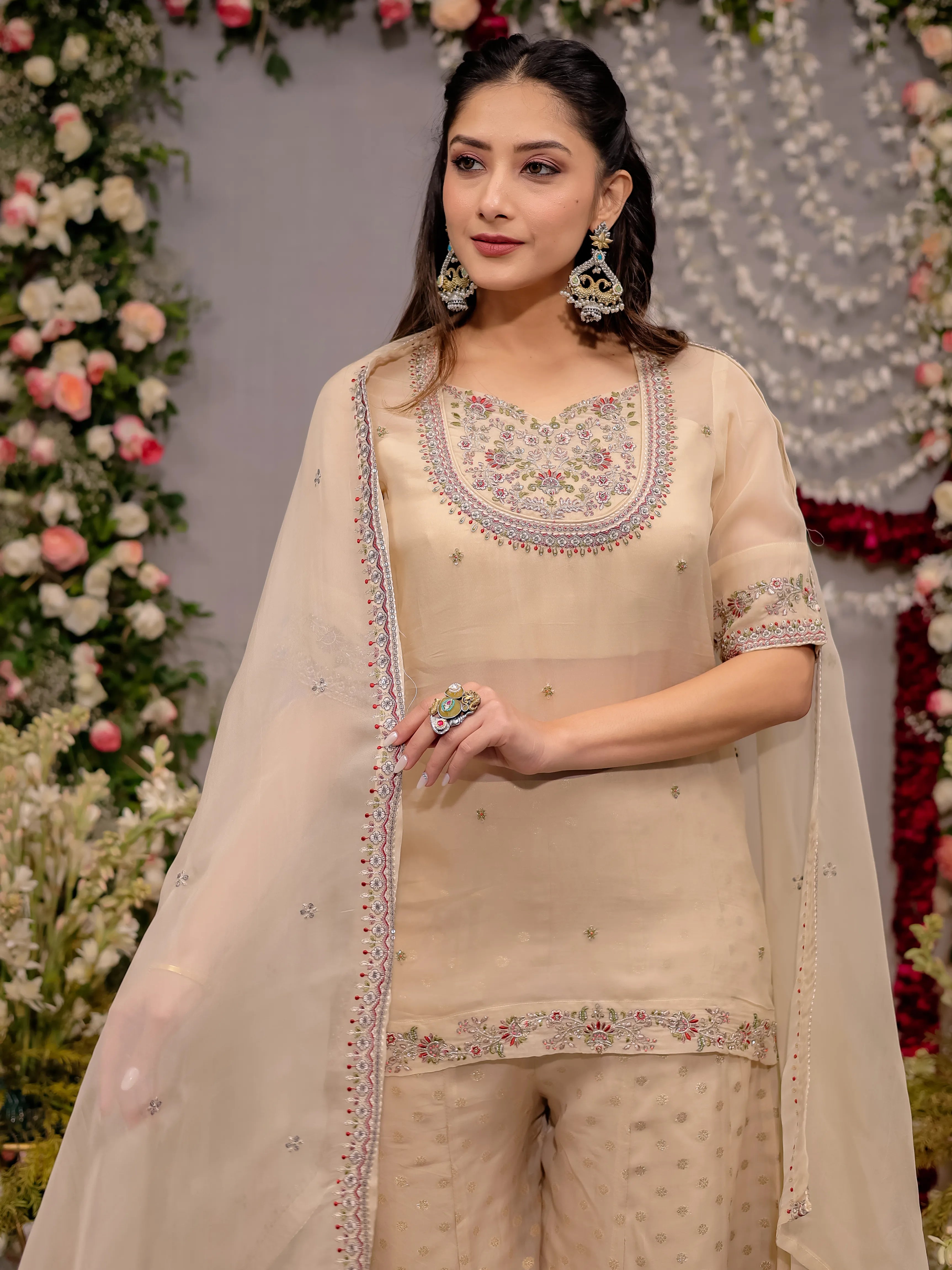 Woman in a beige embroidered outfit standing in front of floral decorations