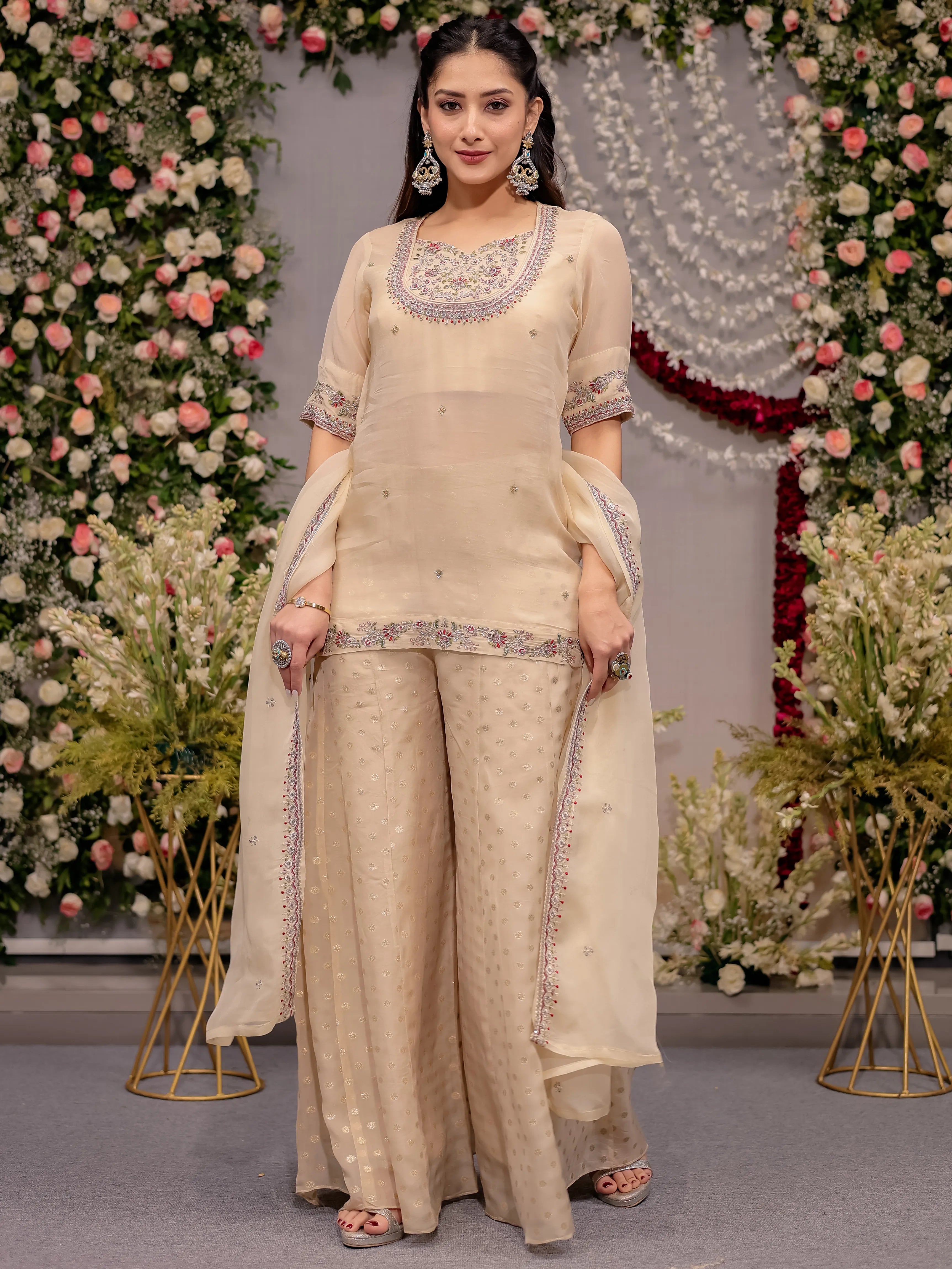 Woman in a beige traditional outfit with floral decorations in the background
